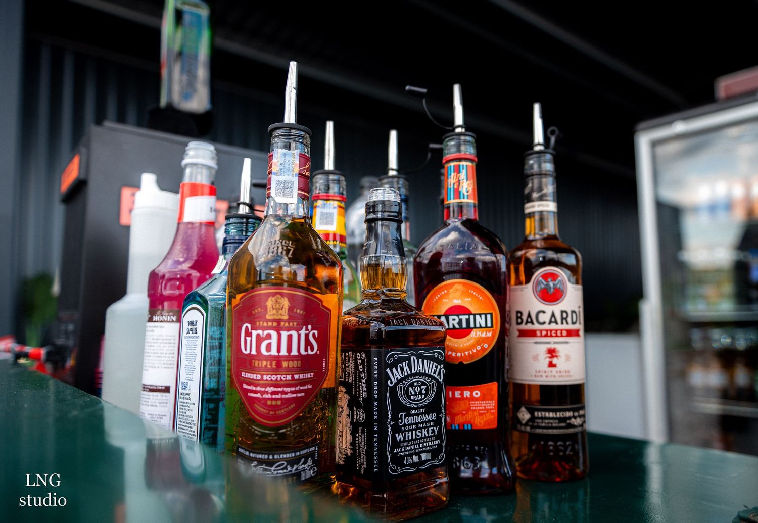 Row of various liquor bottles displayed on dark shelf with moody lighting.