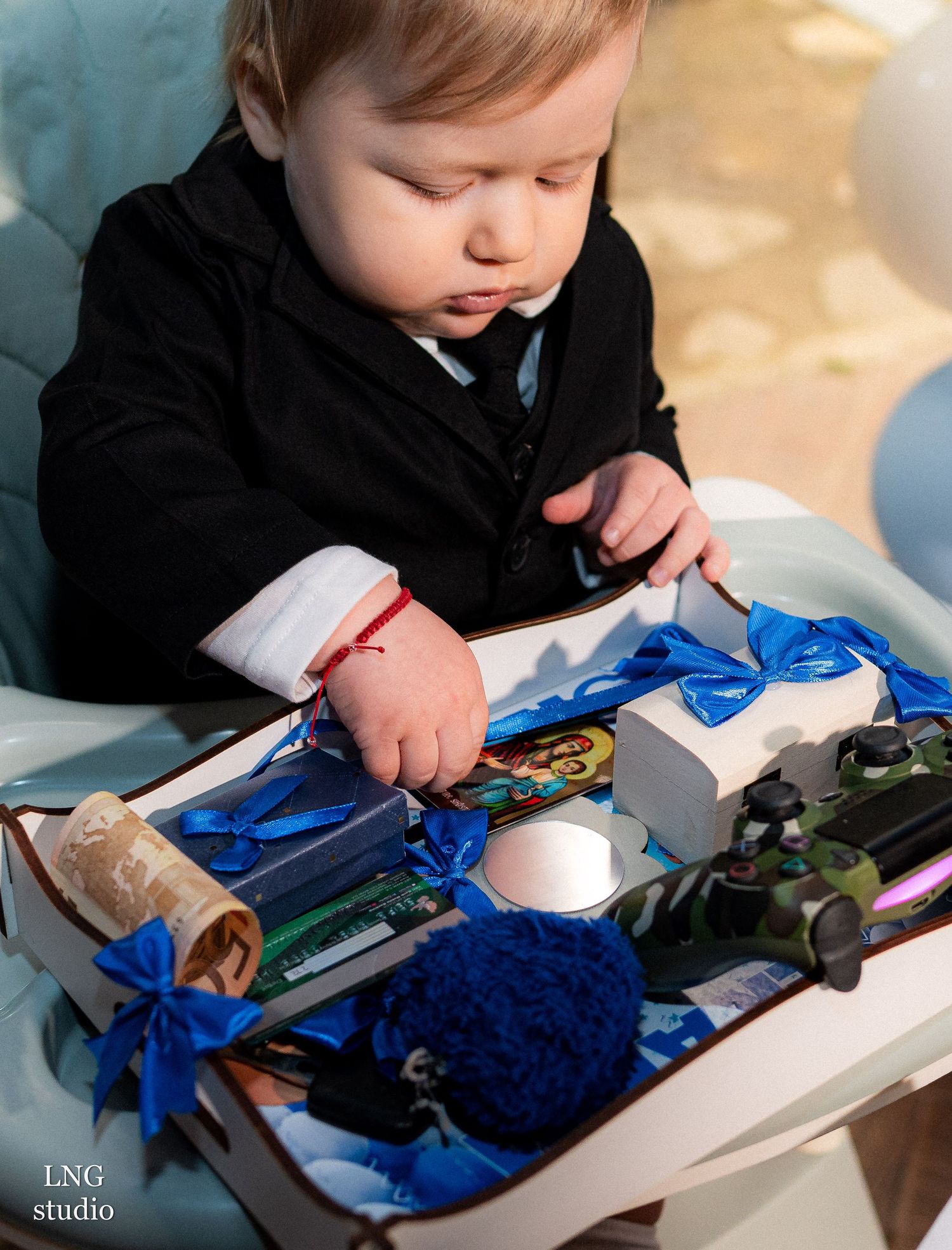 Small child in black formal outfit examining wrapped presents and party decorations.