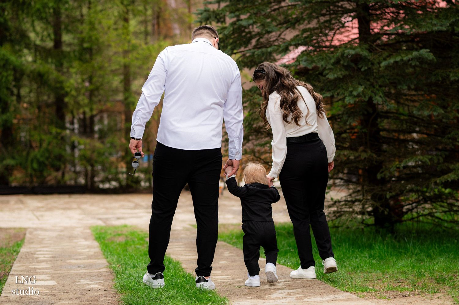 Family walking together hand in hand on outdoor path wearing matching black and white outfits.