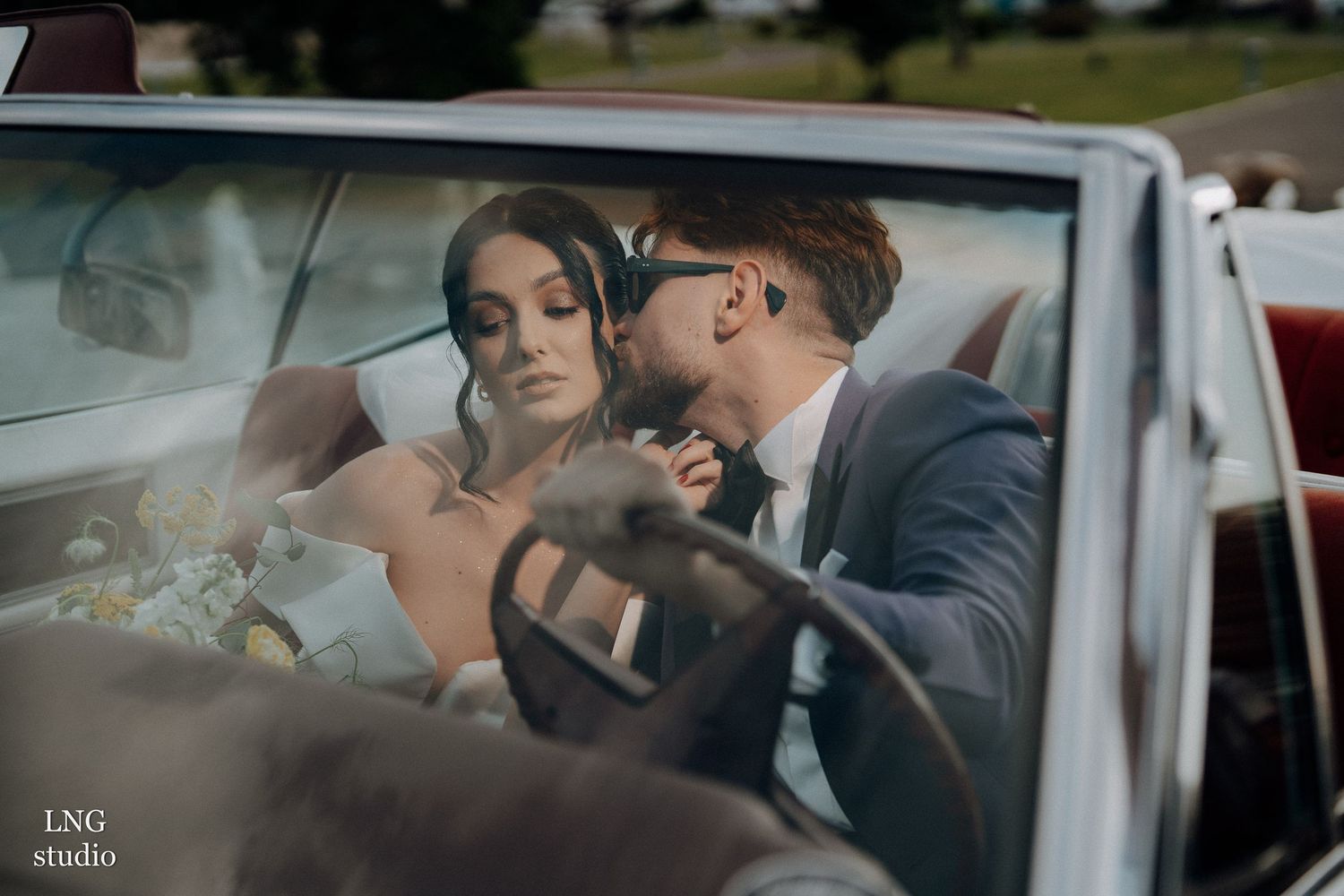 A couple shares an intimate moment inside a classic car on their wedding day.