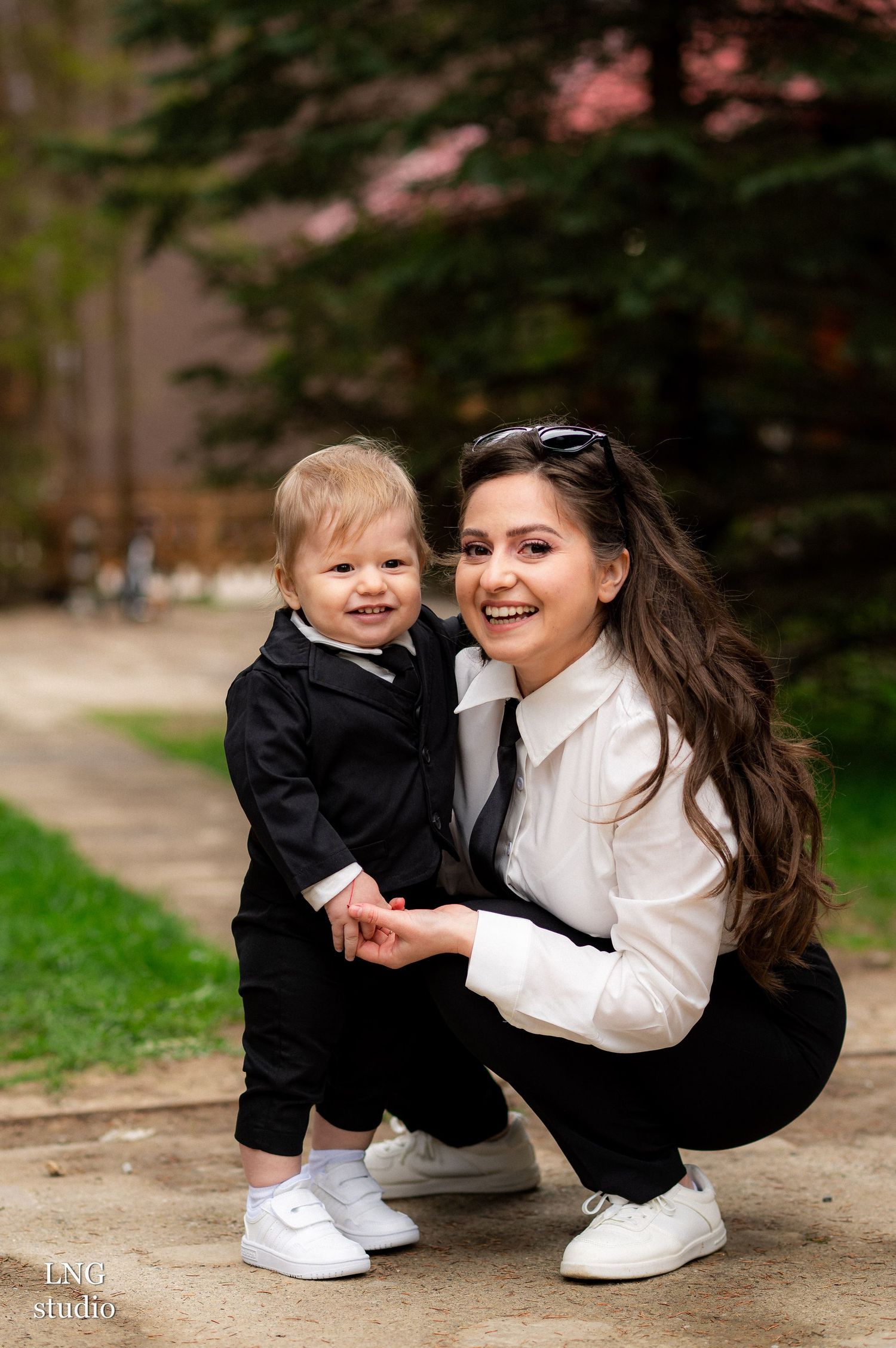 Sweet moment between parent and child wearing matching black and white formal outfits outdoors.