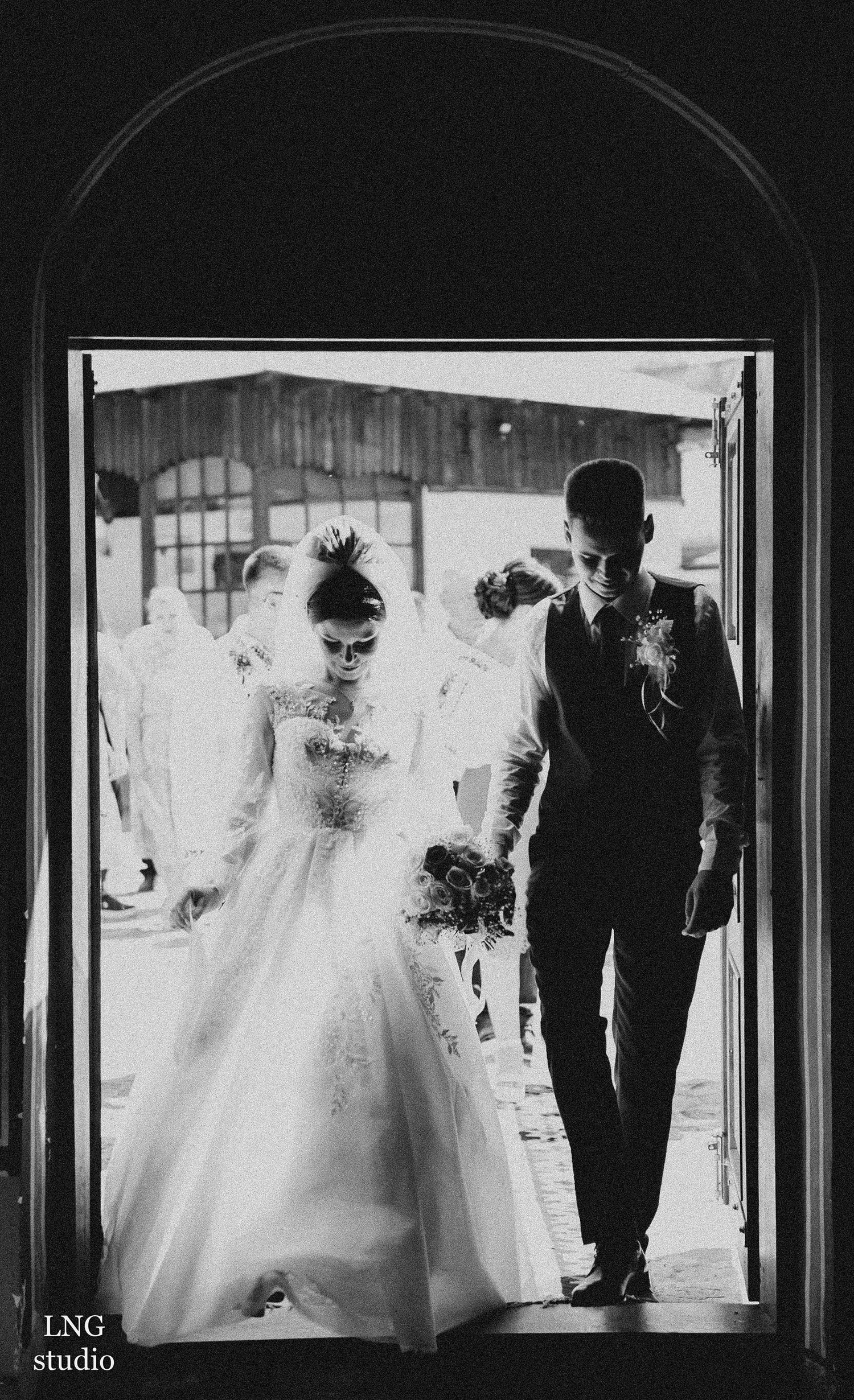 Black and white wedding photo of a couple entering through an arched doorway.