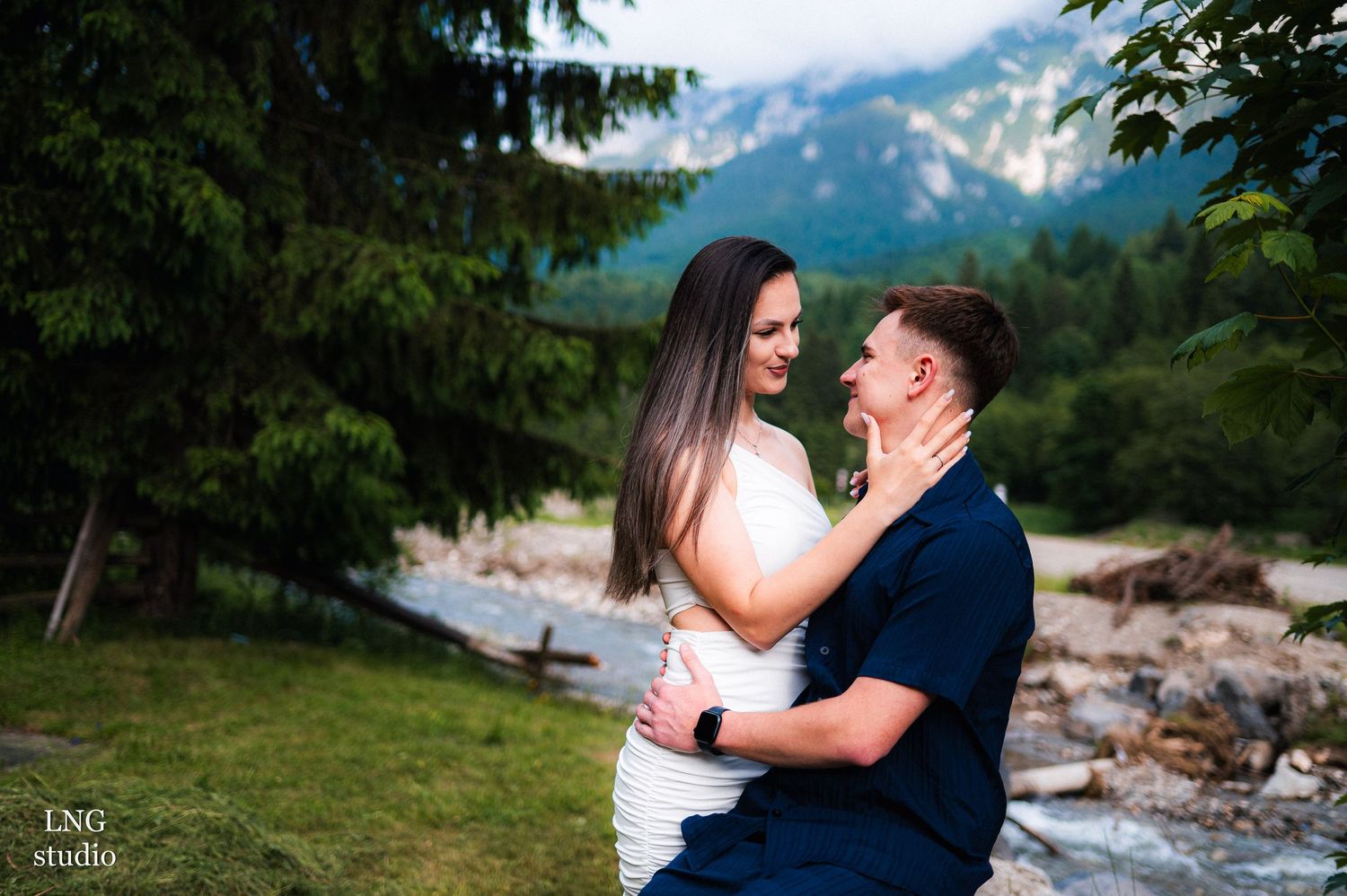 A joyful couple embraces during their mountain photoshoot by a stream.
