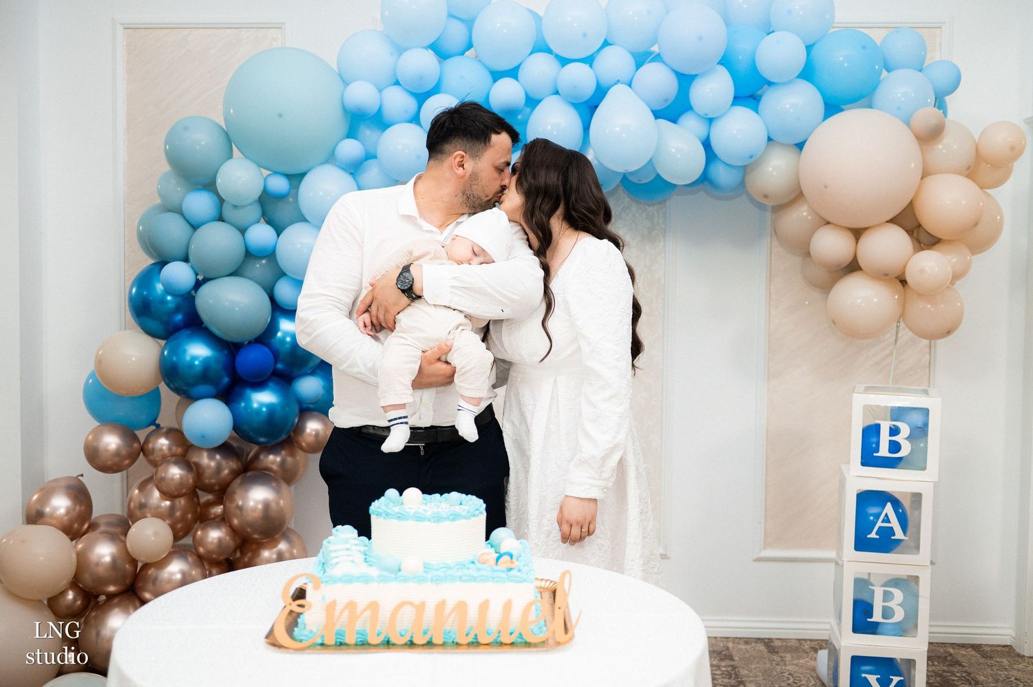 A baby celebration featuring blue and beige balloon garlands with a white cake and decorative blocks.
