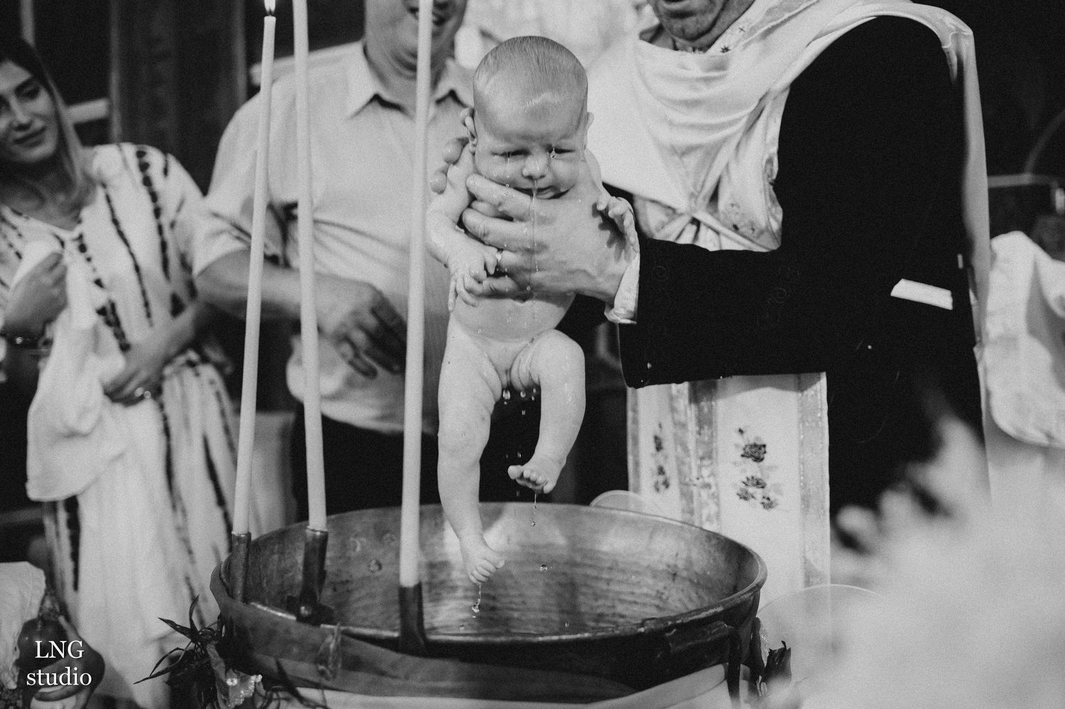 Black and white photo of religious baptism ceremony with candles and traditional dress.