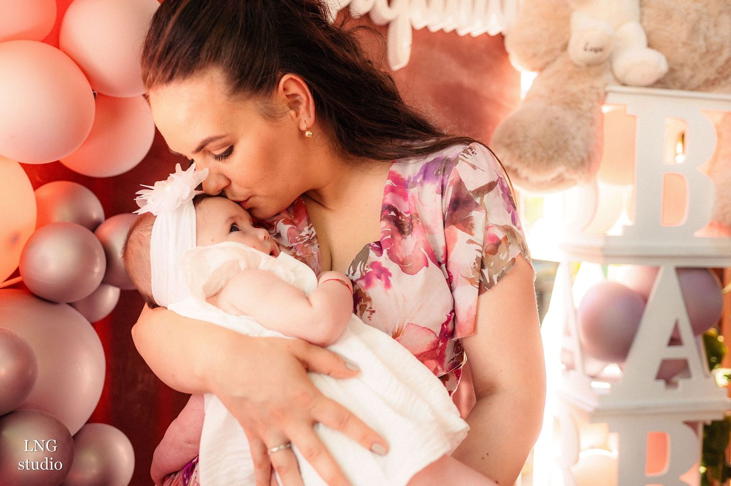 A tender moment with a baby surrounded by pink and purple balloon decorations.