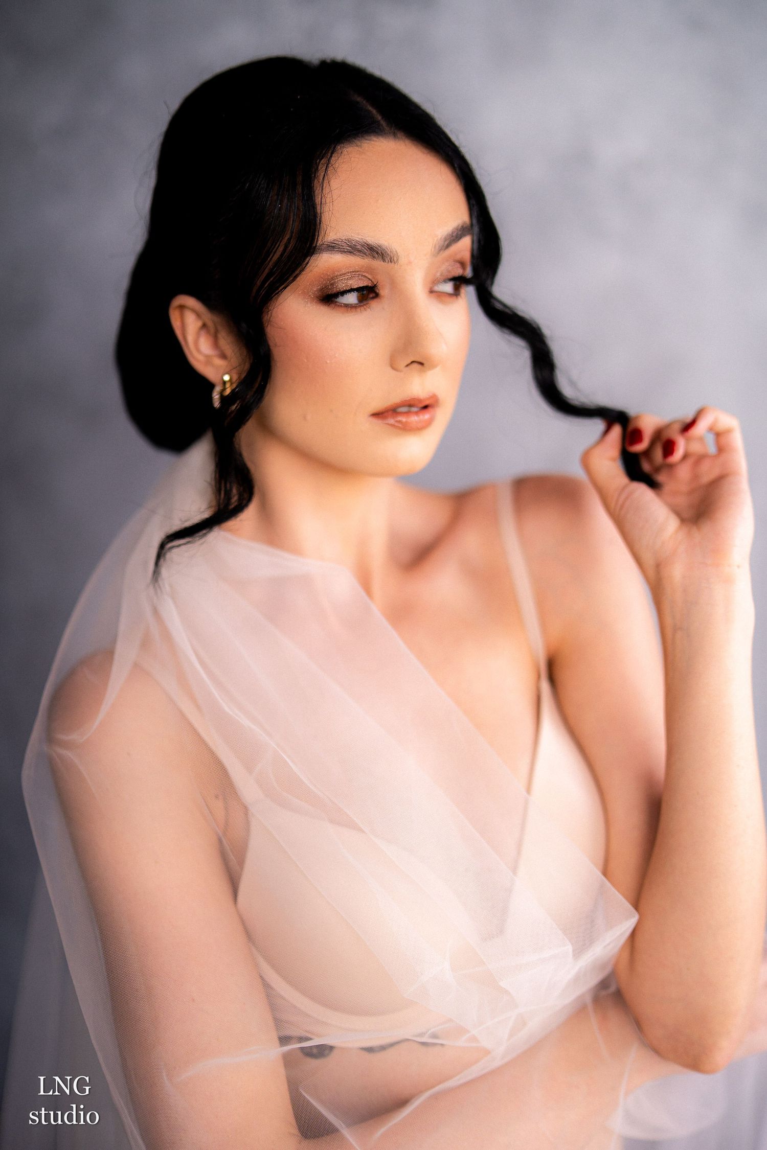 Soft and ethereal portrait featuring sheer fabric, delicate lighting, and romantic styling against a misty gray backdrop.