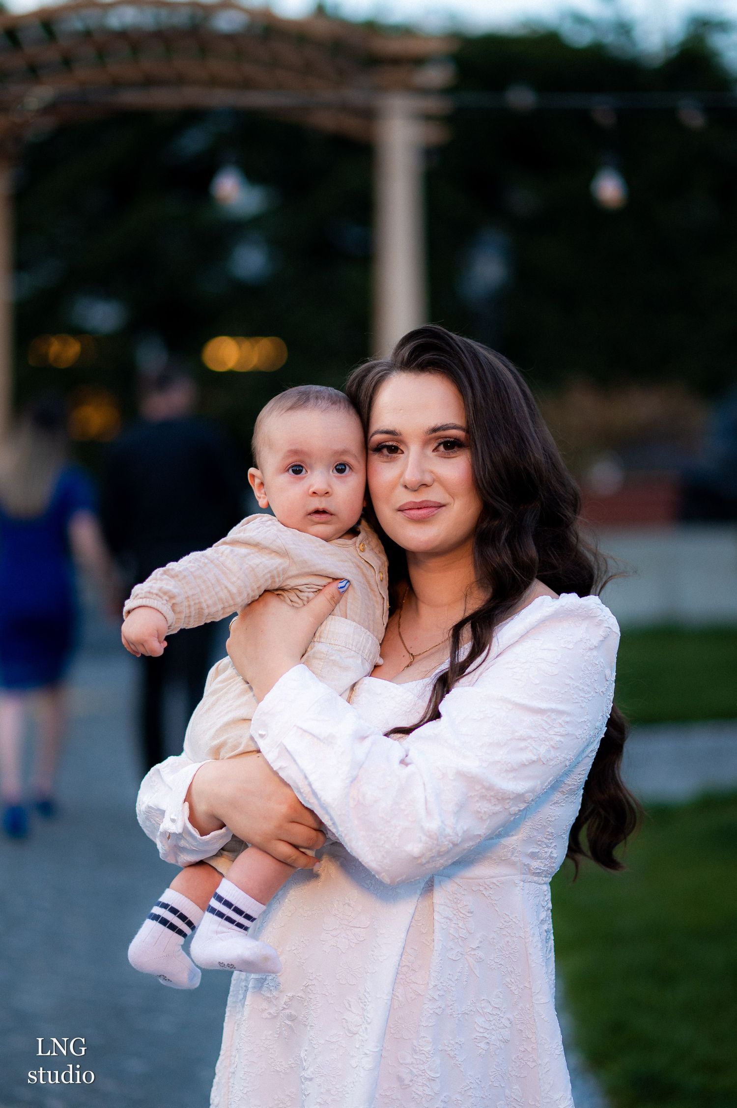 Tender outdoor portrait in white attire beneath a decorative gazebo at dusk.