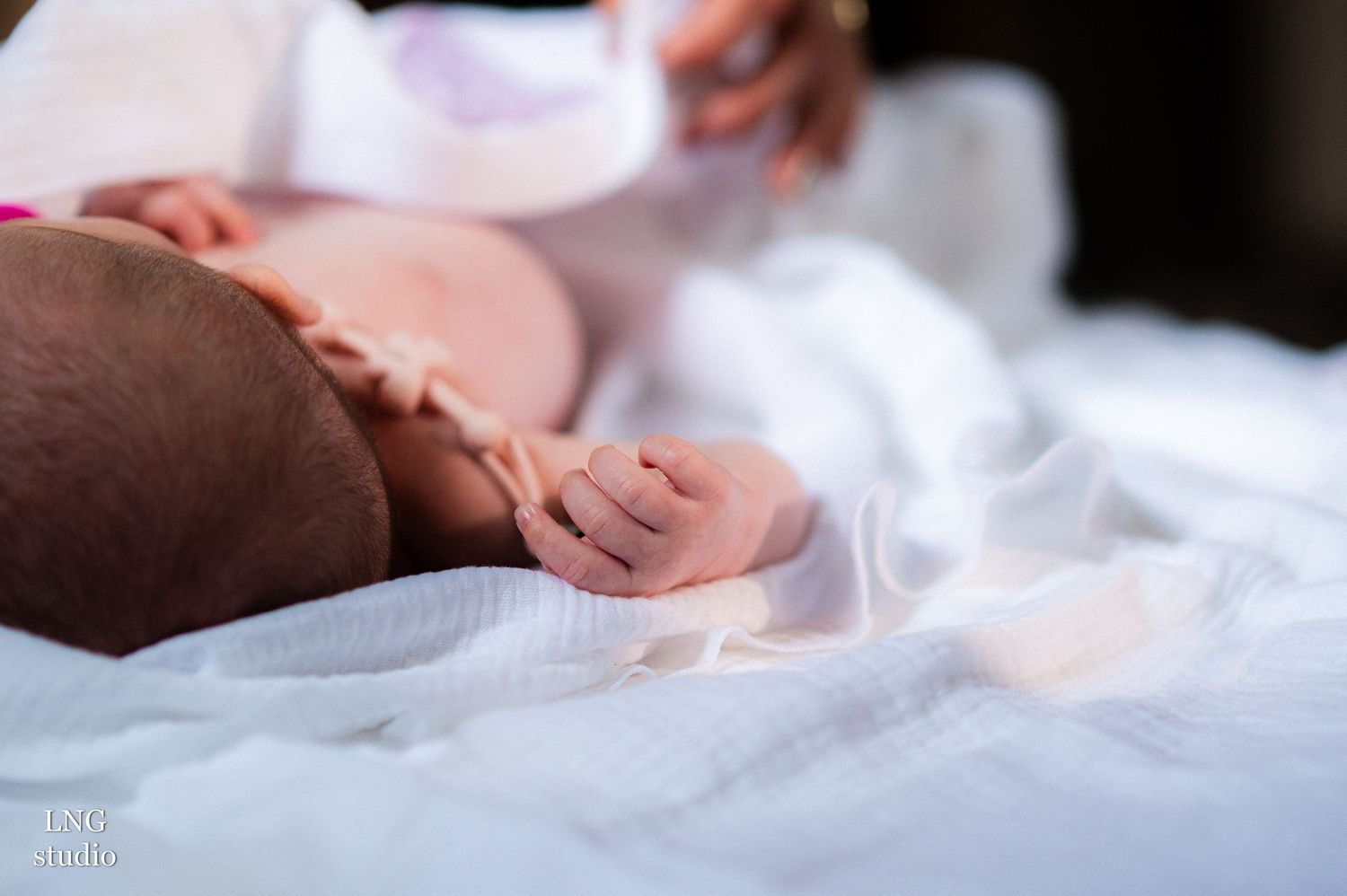 A close-up shot of a newborn baby's hand against white fabric during a baptism ceremony.
