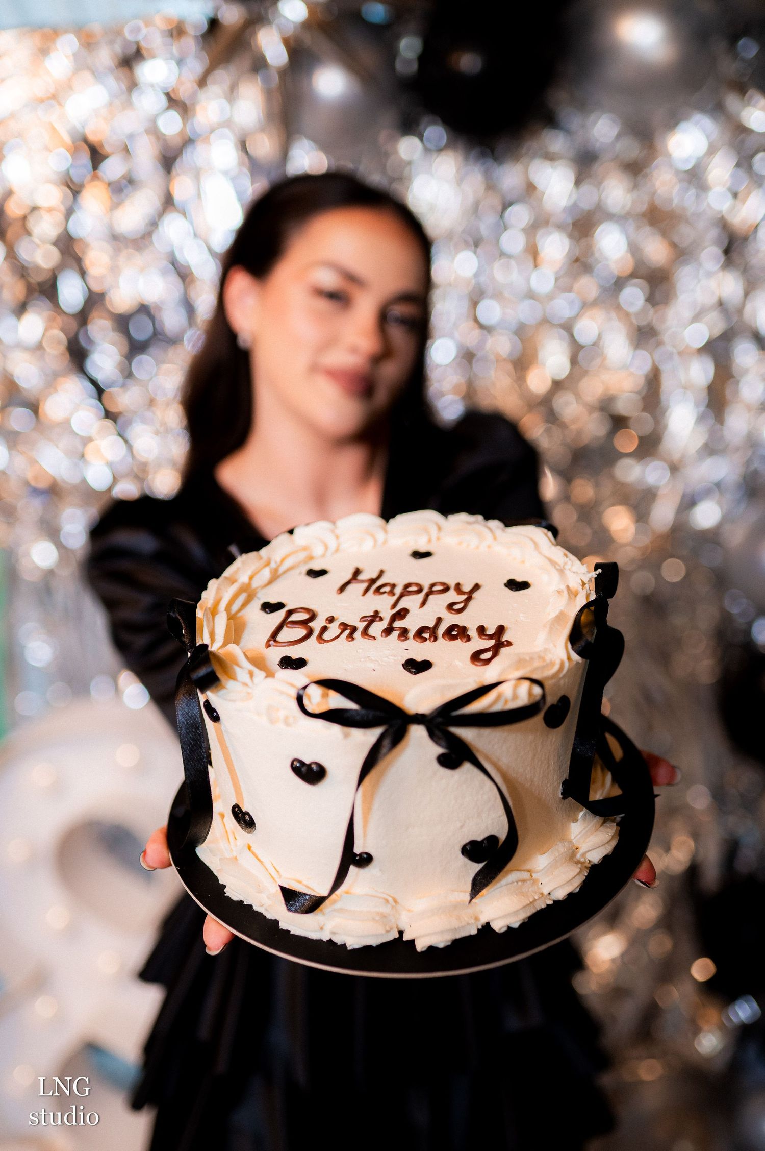 Four connected photos showing someone celebrating with a white birthday cake against a sparkly silver backdrop.