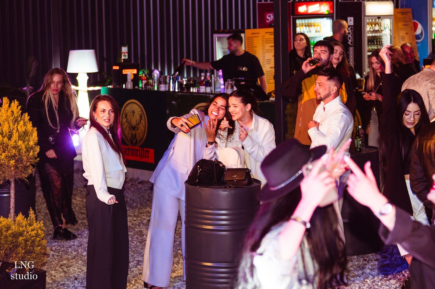 People dancing and celebrating at nightclub with purple ambient lighting.