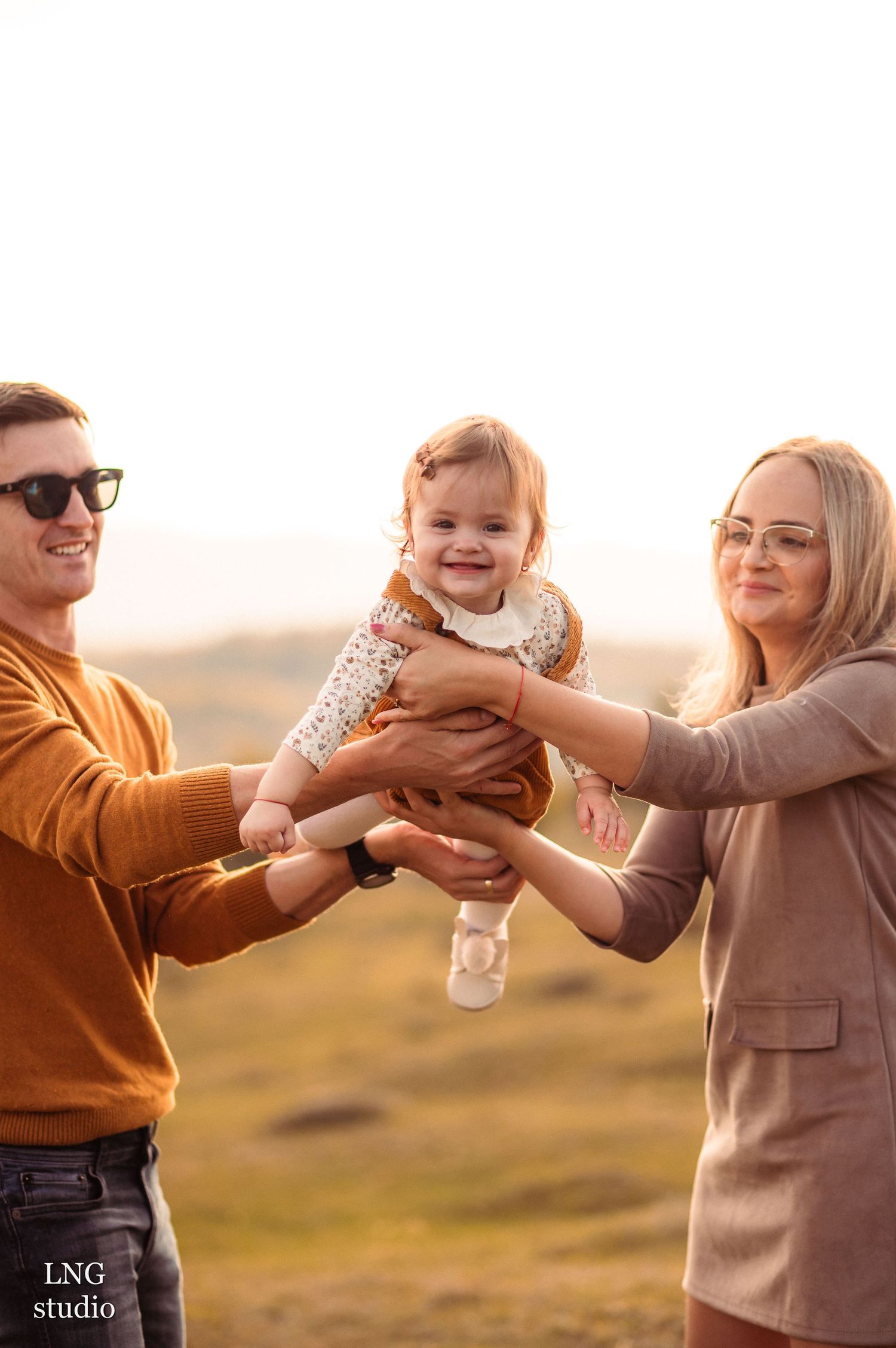 Parents share joyful moment with toddler during outdoor family photoshoot.