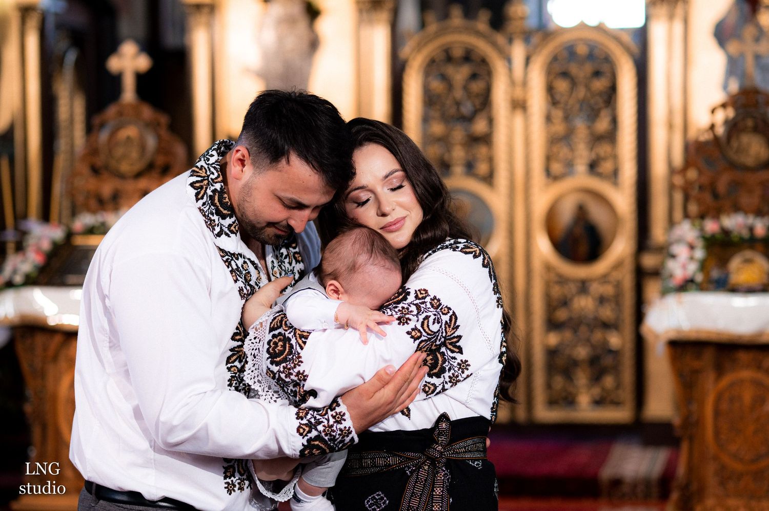 Tender family moment during a christening ceremony with traditional embroidered outfits.