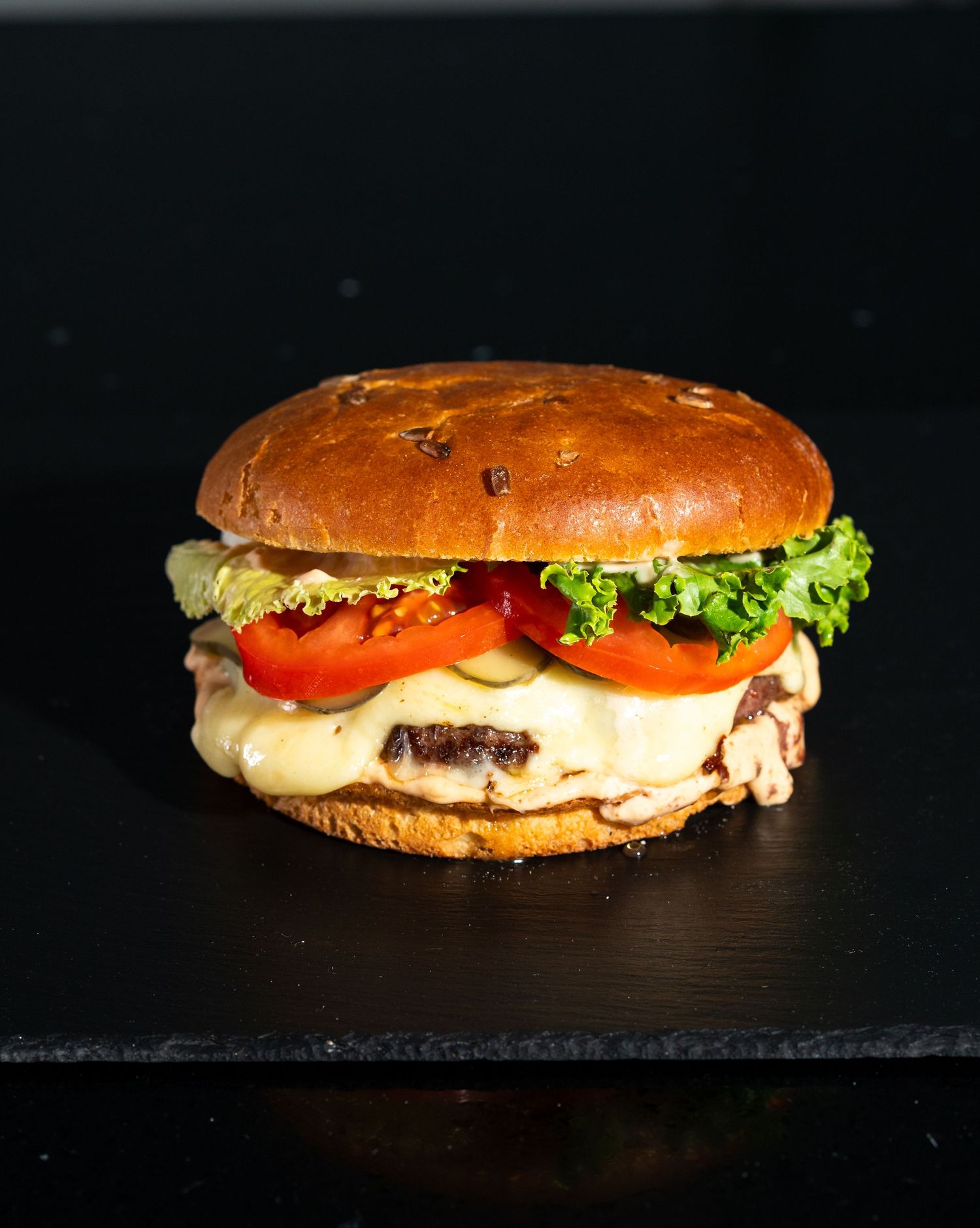 Gourmet hamburgers with fresh toppings lined up on dark surface with dramatic lighting.
