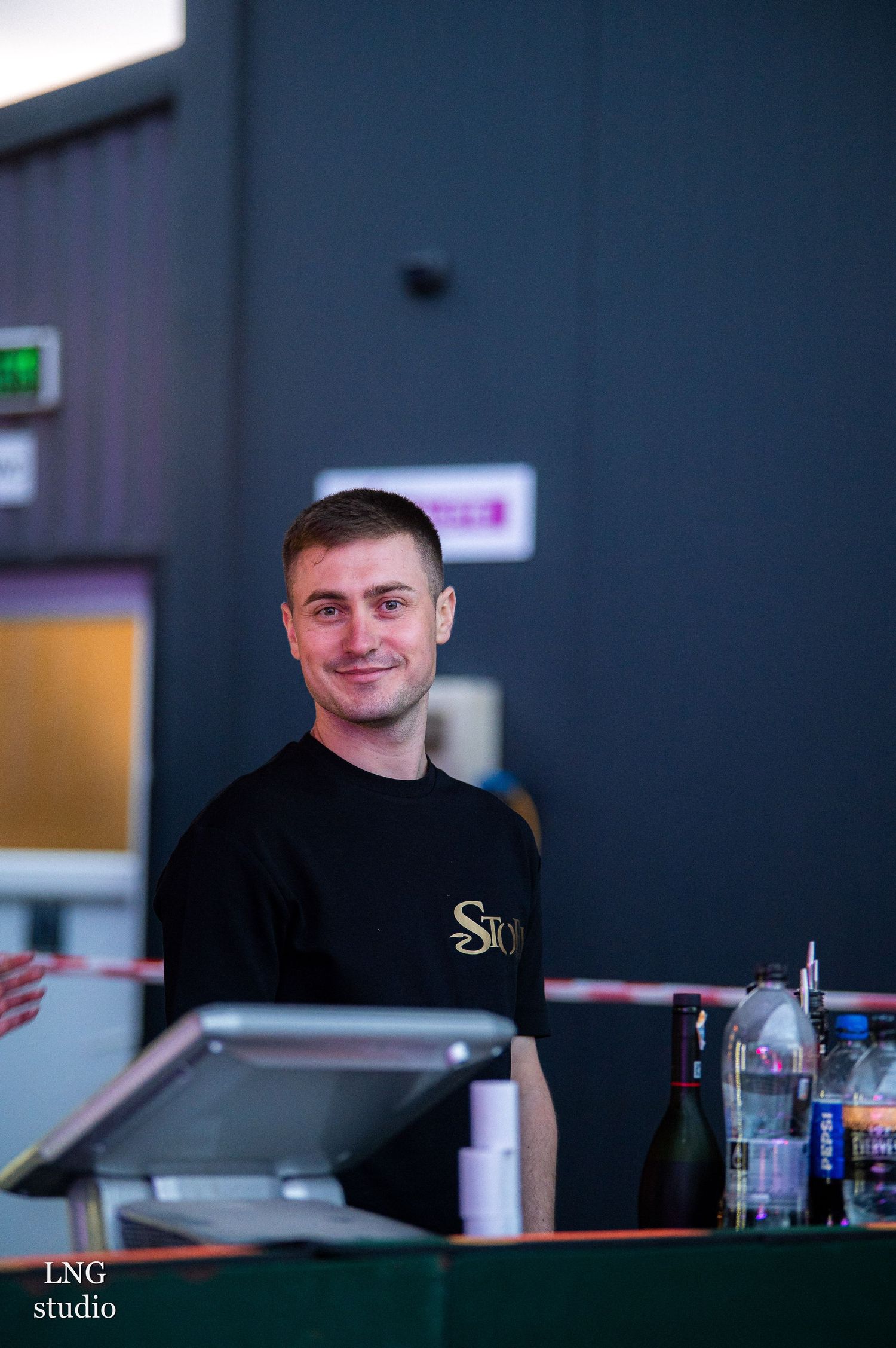 Staff member in black uniform stands behind counter at food service station during evening service.