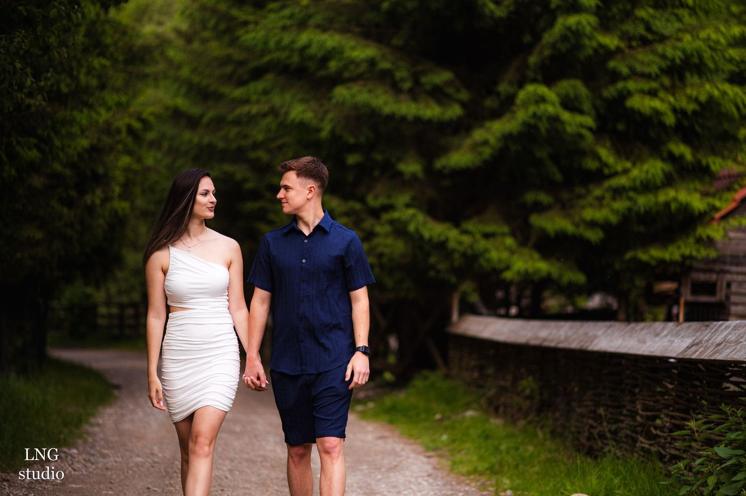 Couple walking side by side on gravel path surrounded by lush green forest.