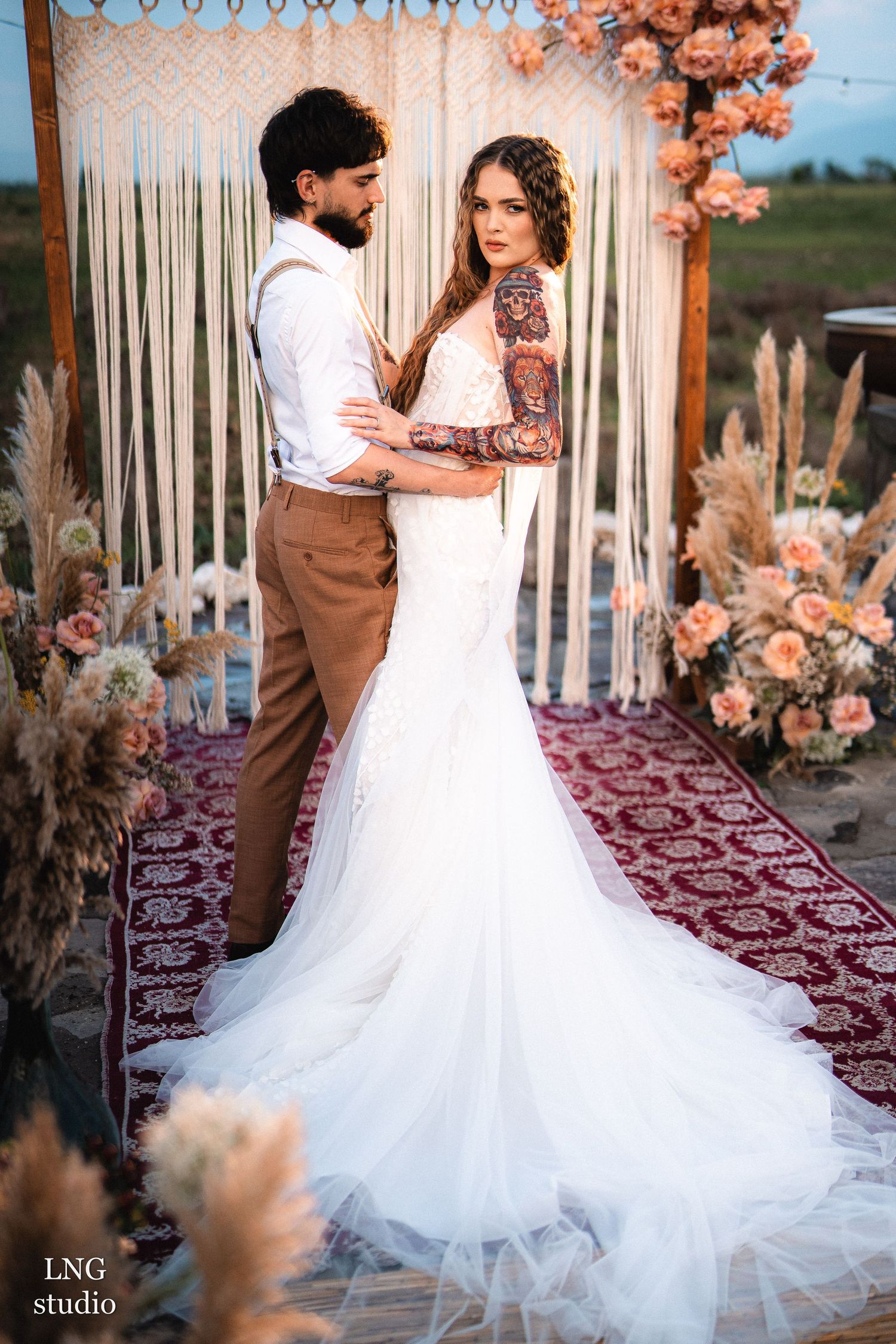 Romantic wedding couple posing at sunset with floral decorations and pampas grass under a rustic bamboo arch.