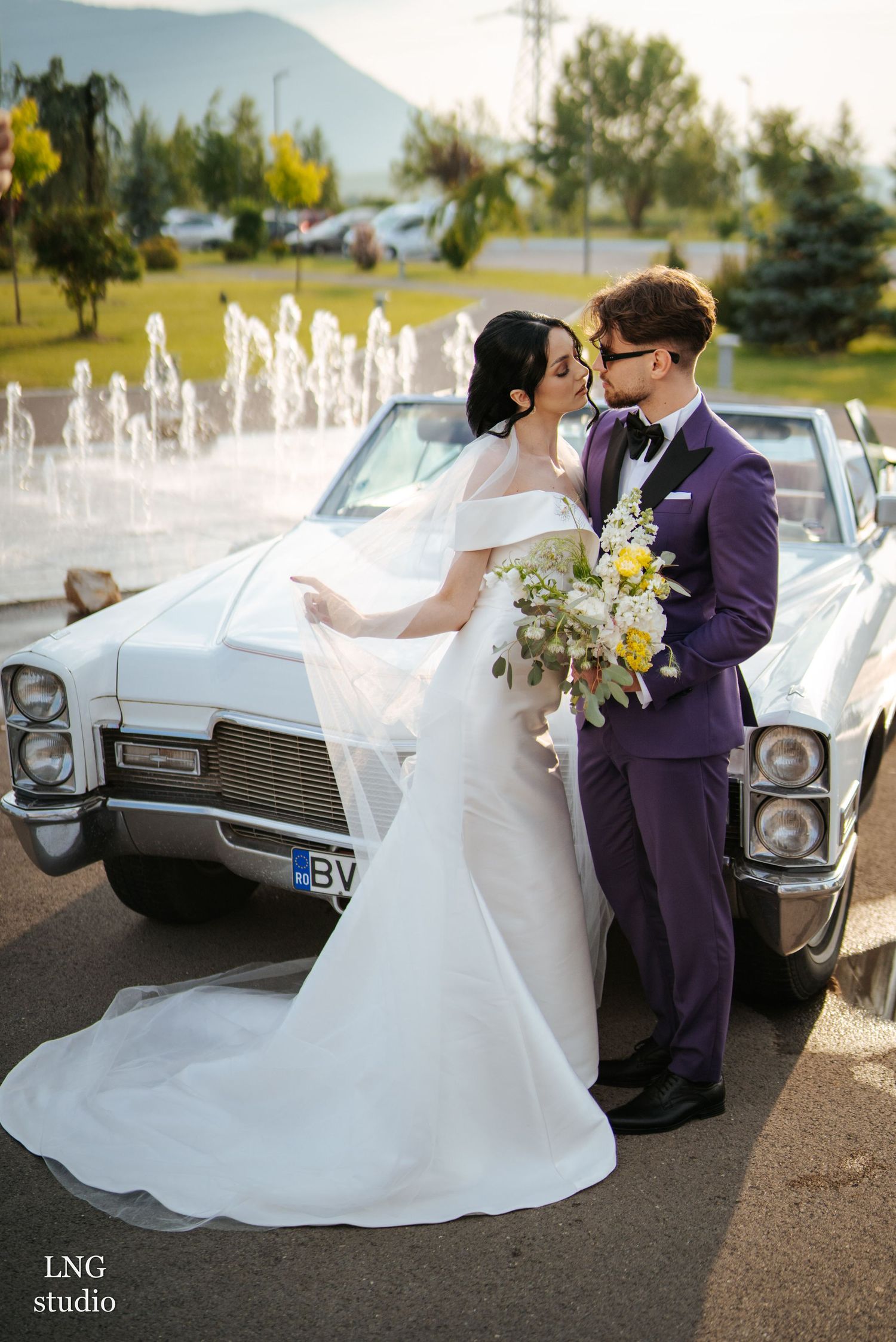 Wedding photoshoot with a white vintage car featuring elegant bridal attire and purple accents.