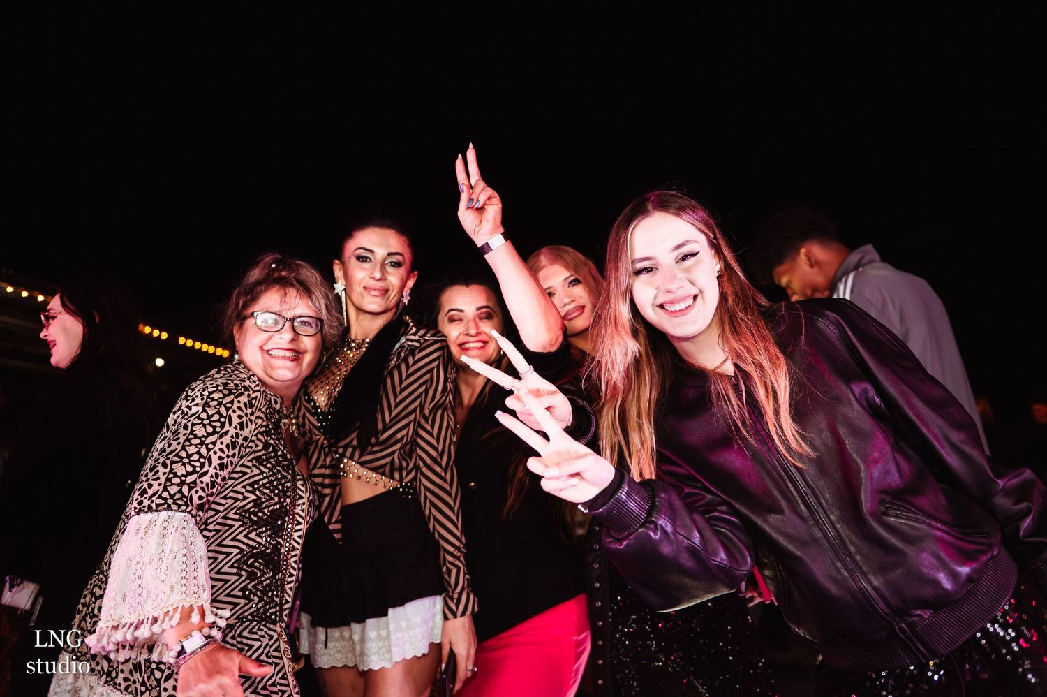 Group enjoying a nighttime entertainment event with bright stage lights in background.