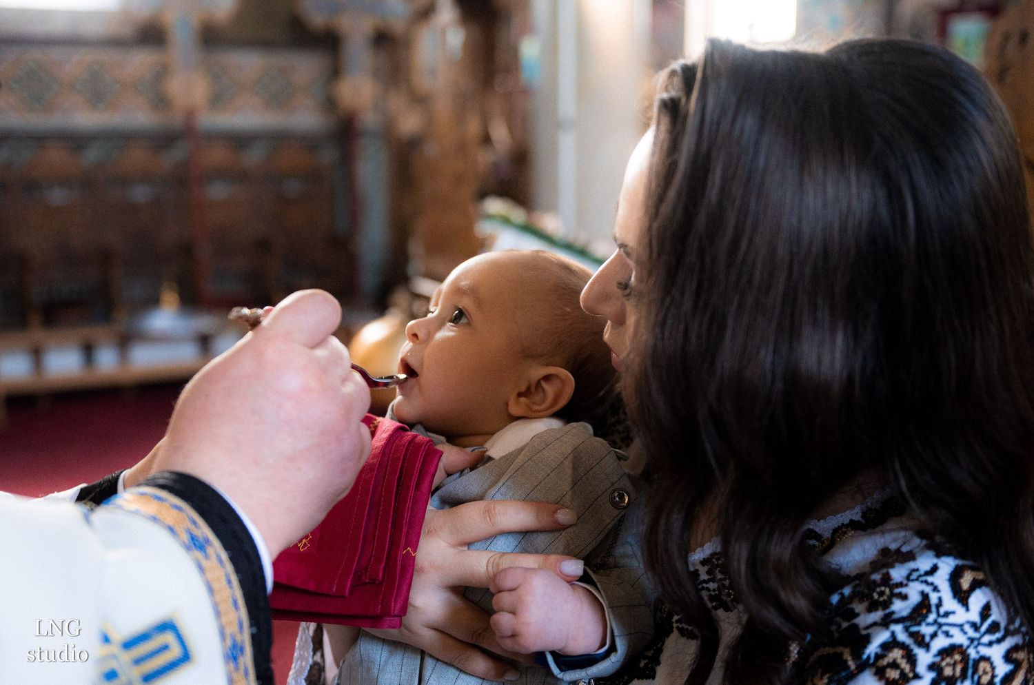 Baby receiving communion during an Orthodox Christian baptism ceremony in a traditional church setting.