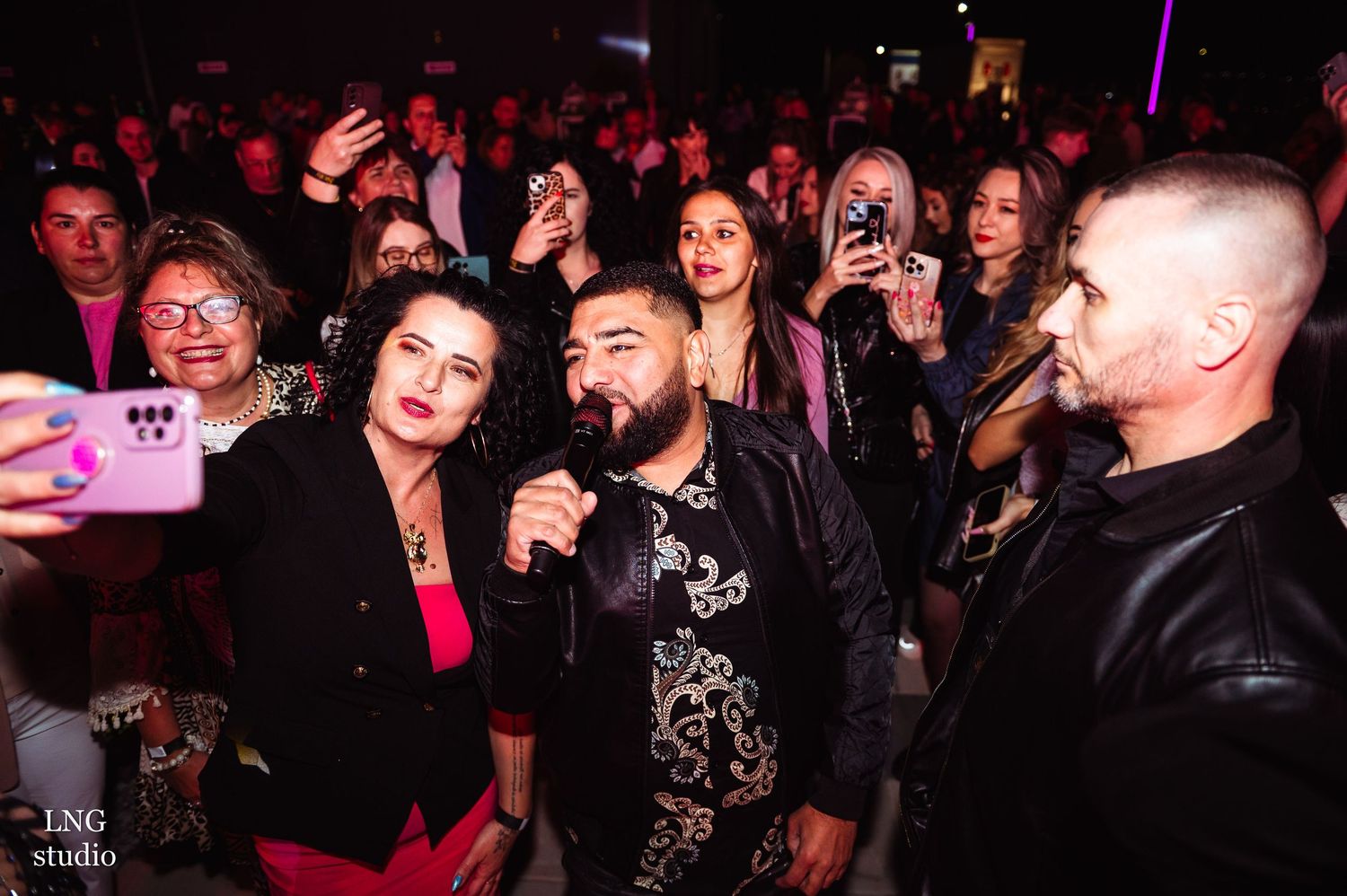 Energetic crowd at a nightclub event with colorful lighting and mobile phones raised.