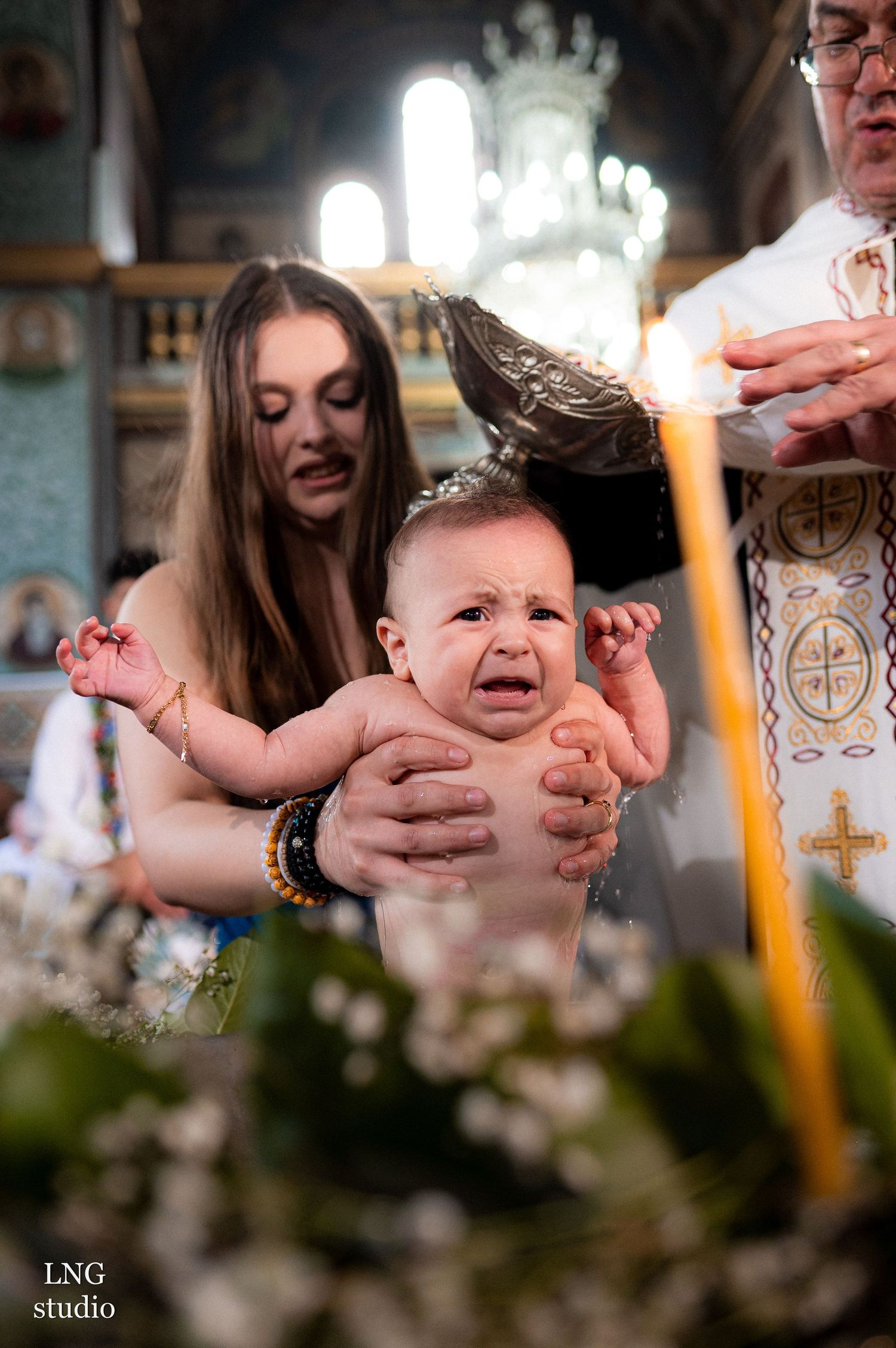 Emotional moment during Orthodox baptism ceremony with candles and religious icons.