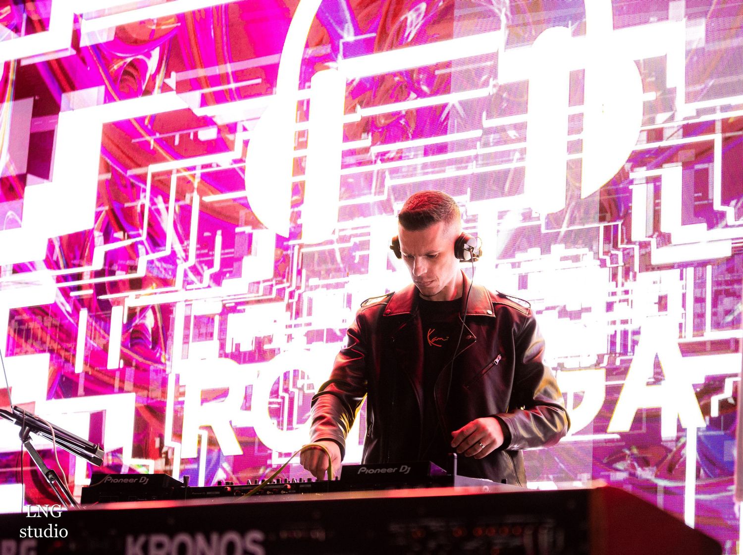 DJ performing at an event with vibrant pink geometric light display backdrop.