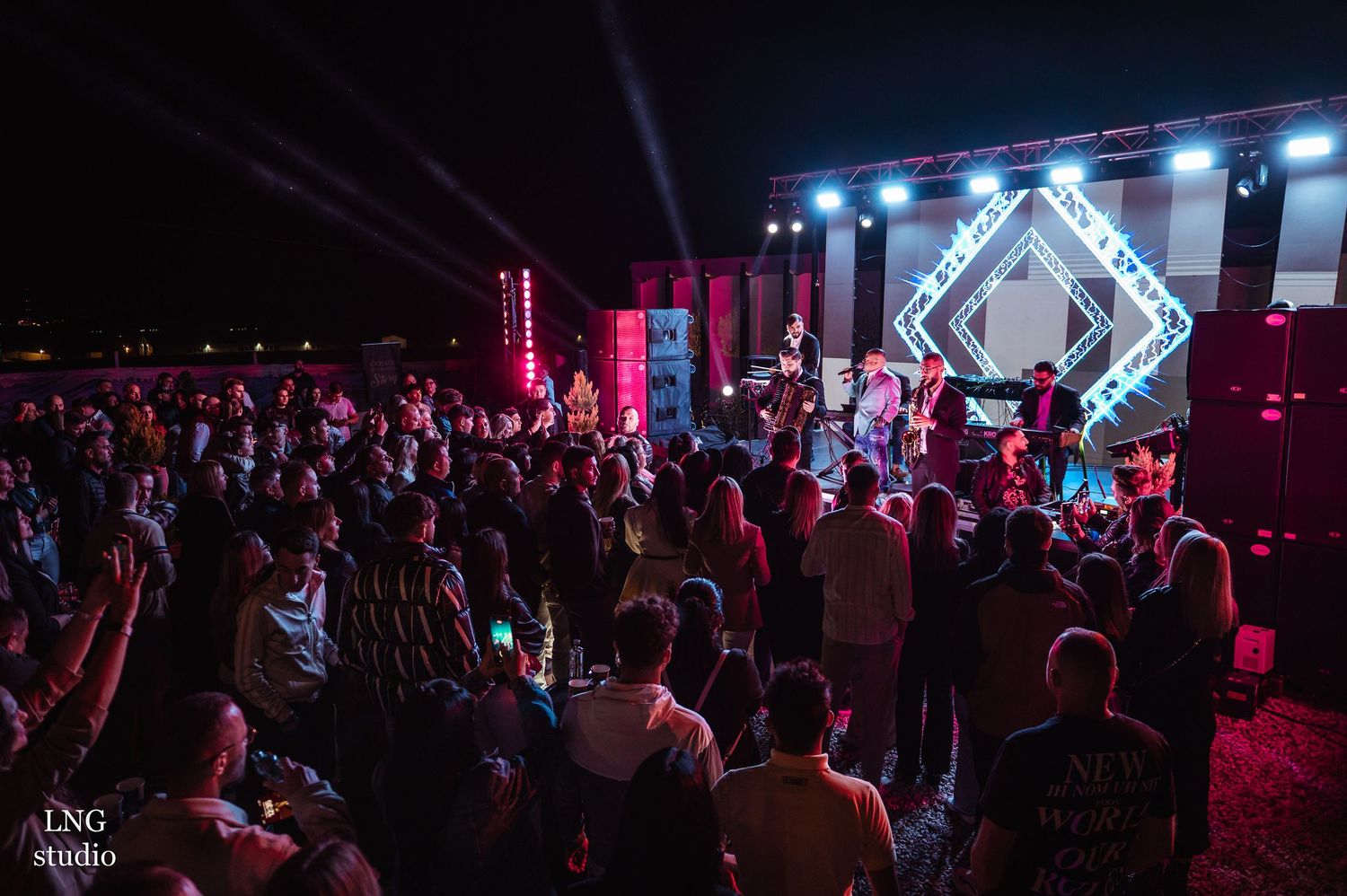 Concert crowd faces illuminated stage with geometric light display and pink lighting effects.