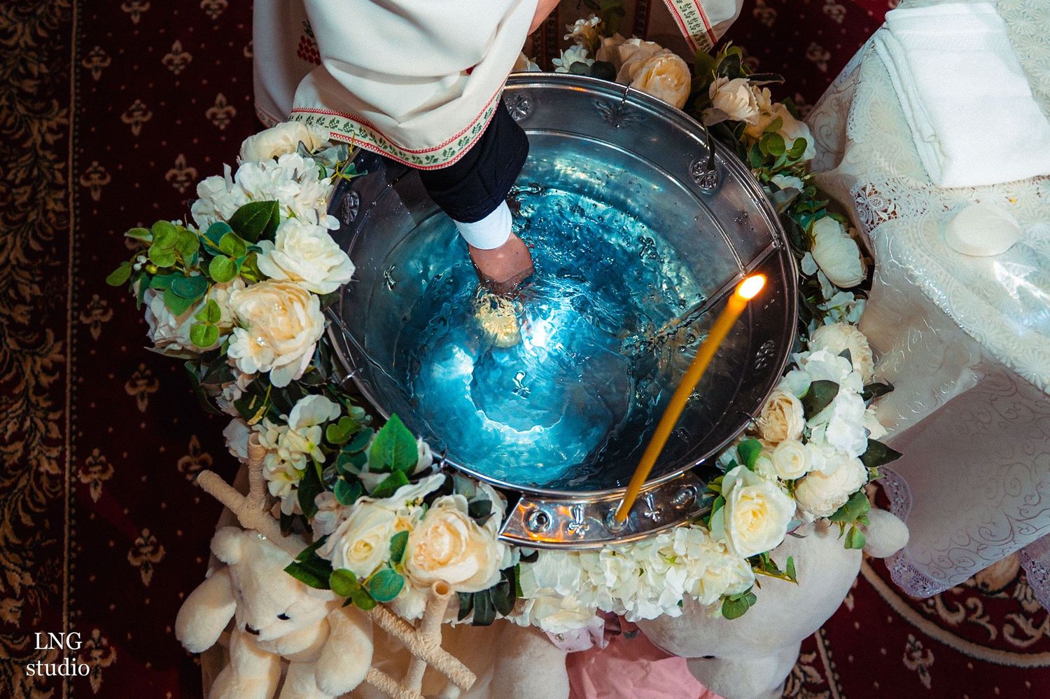 Blue baptismal font decorated with white roses and plush toys.