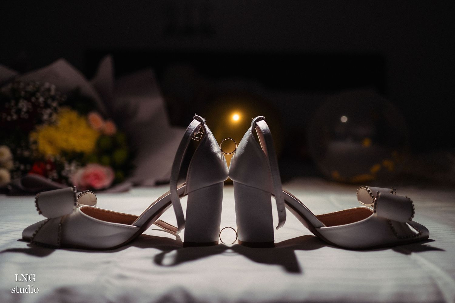 Artistic composition of wedding shoes and accessories in dark moody lighting.