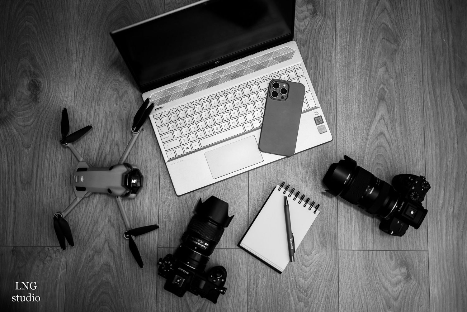 Flat lay of photography equipment including cameras, laptop, and notepad on wooden surface.