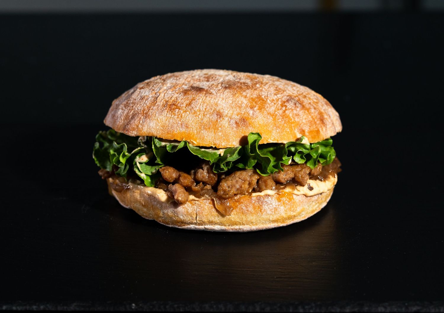 A gourmet sandwich with lettuce and meat on artisanal bread photographed on black surface.