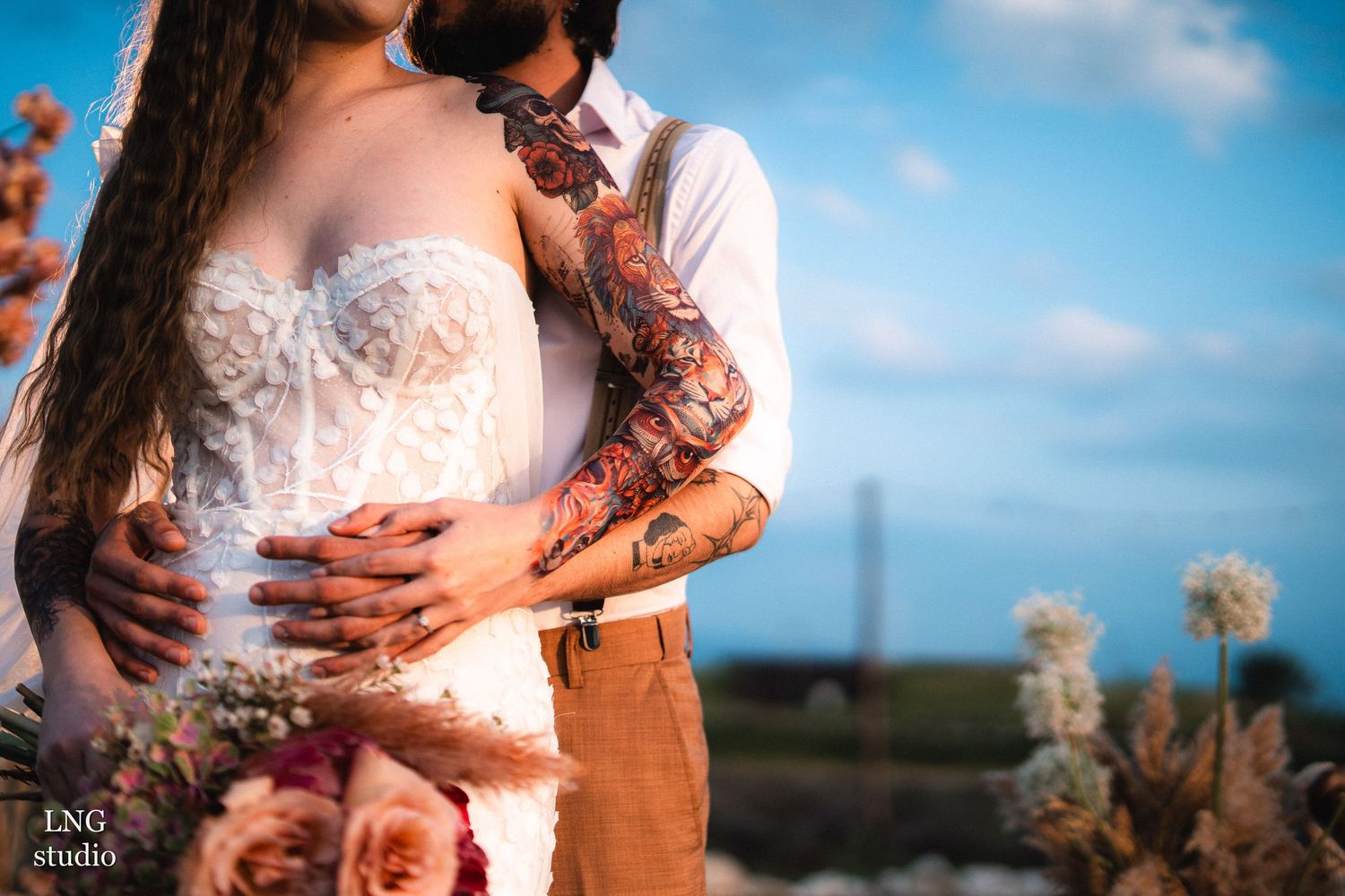 Close-up shot of a couple holding hands outdoors against a vibrant blue sky background.
