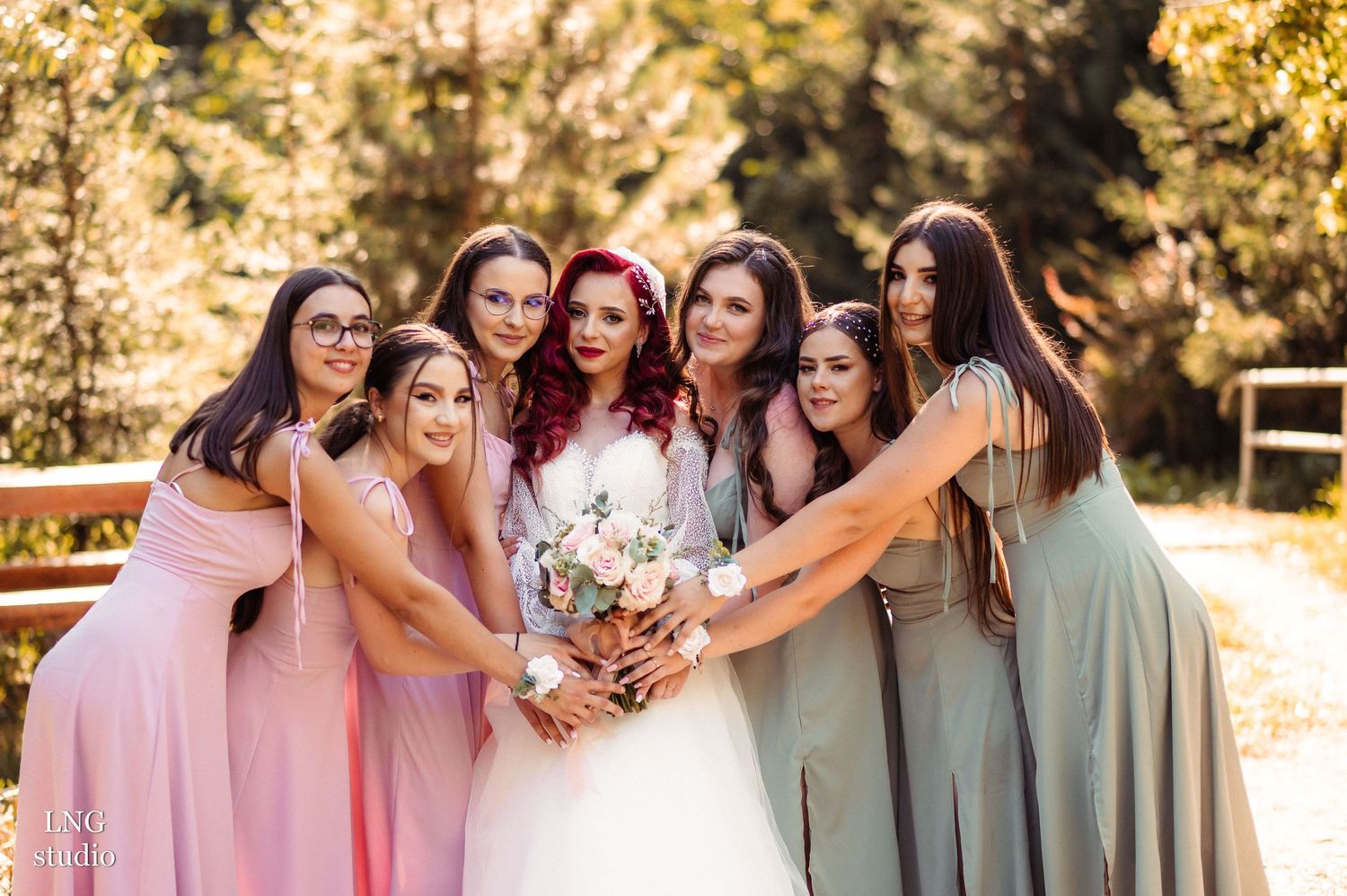 Wedding party members in pink and gray dresses pose together in outdoor golden light.