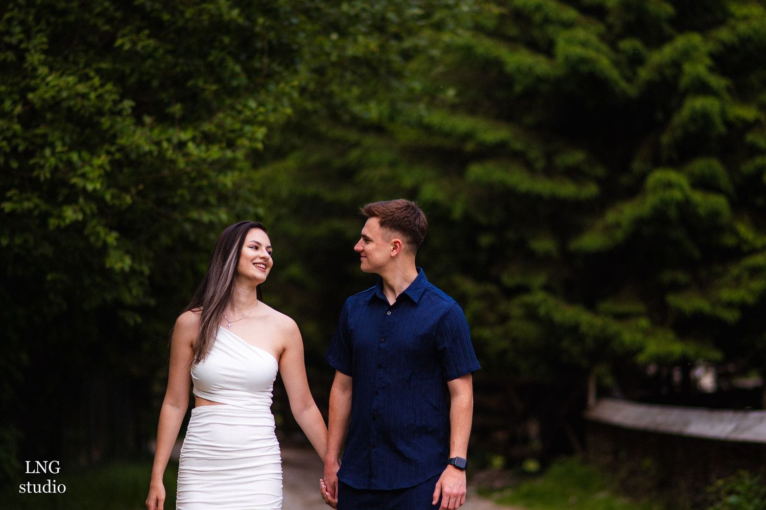Romantic outdoor photoshoot with couple walking along wooded trail.