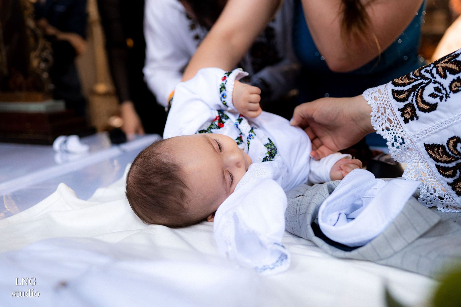 Infant lying on white fabric during religious ceremony.