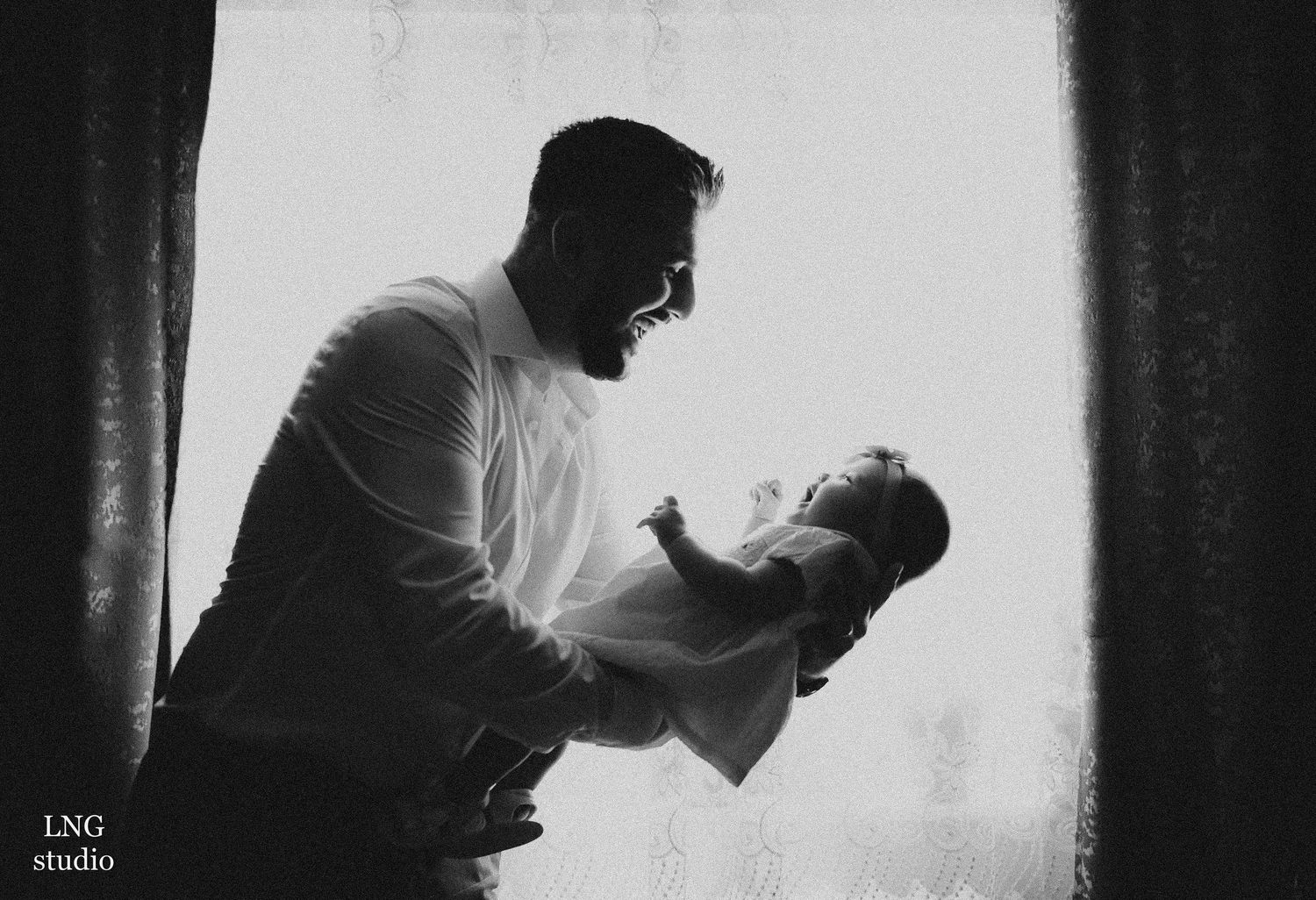A silhouetted figure tenderly holds a baby against a bright window backdrop.