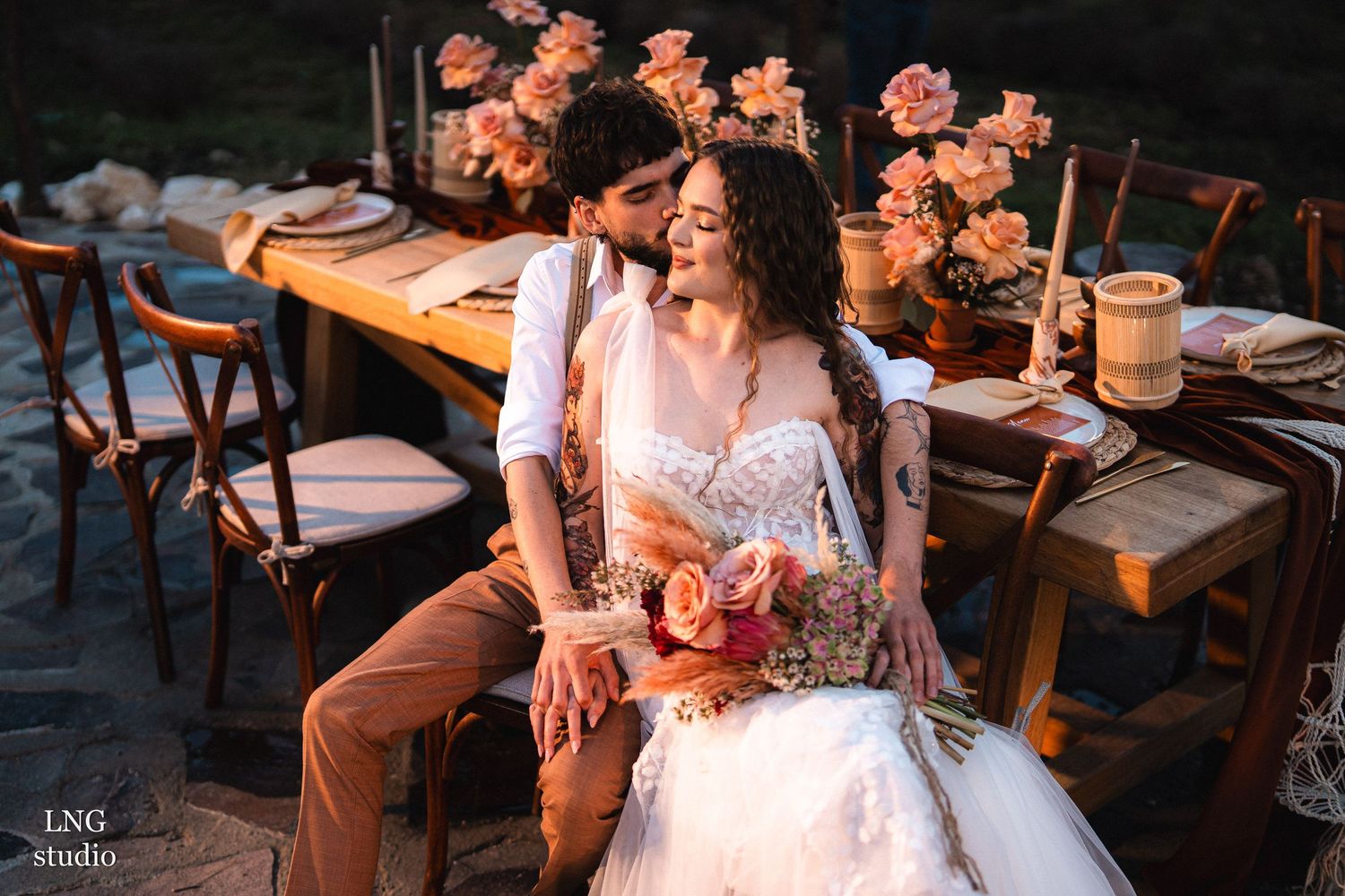 Two floral arrangements with coral and peach roses decorate an elegant table setting in a romantic, dimly lit space.