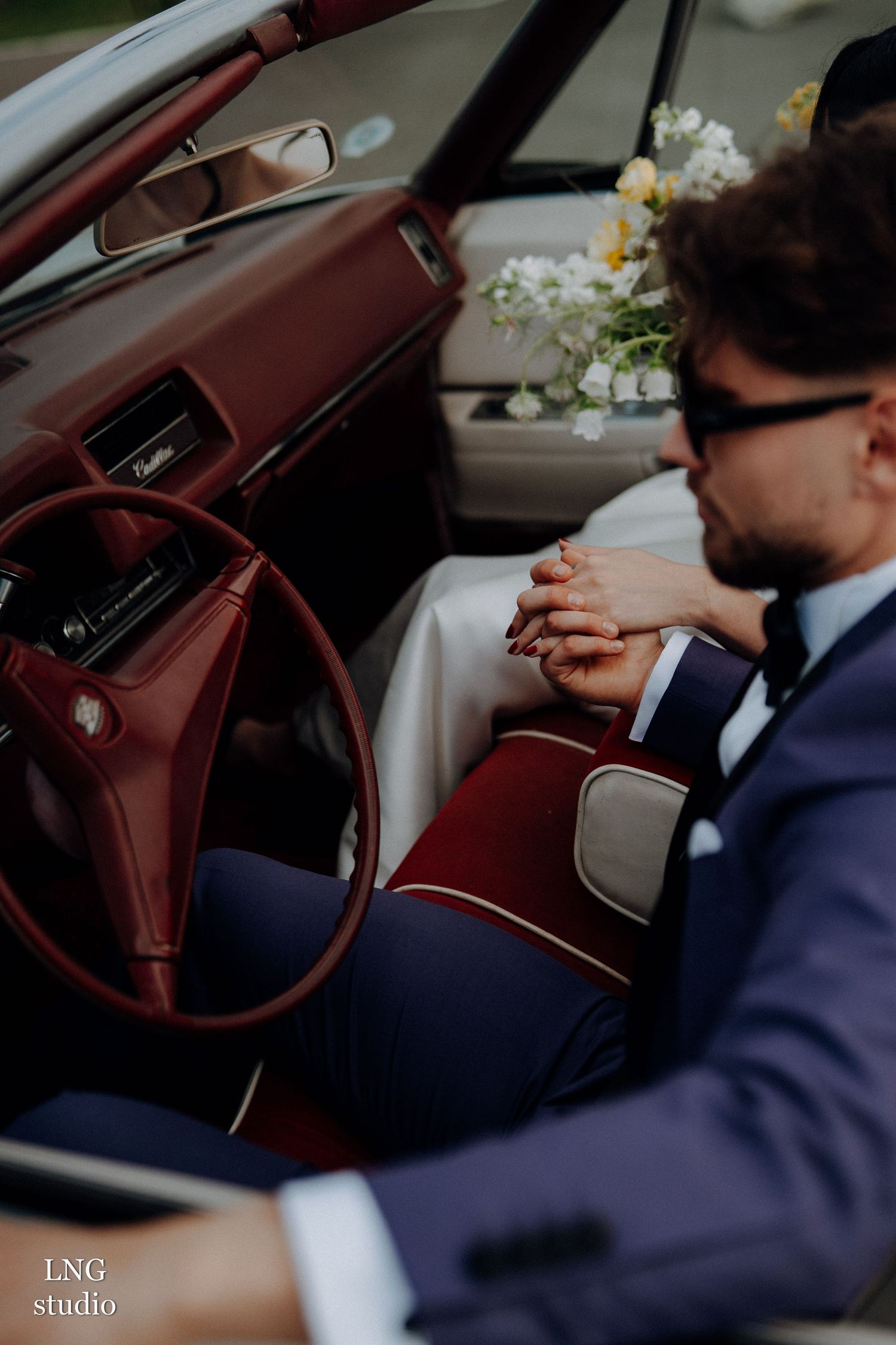 A close-up shot inside a vintage car with burgundy leather interior, showing part of someone in a navy suit.