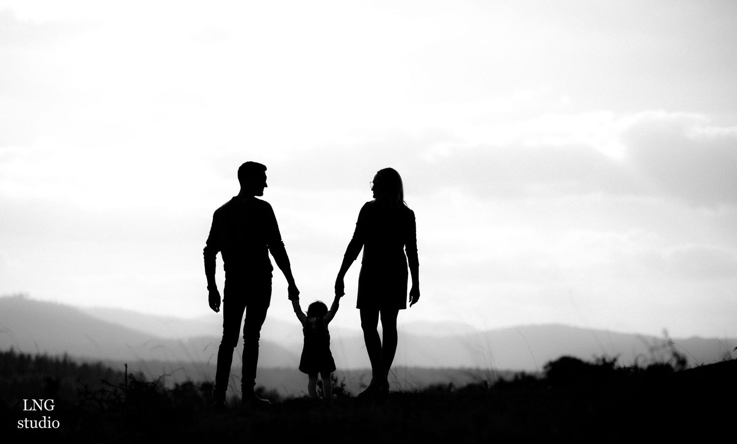 Silhouette of family holding hands against mountain backdrop at sunset.