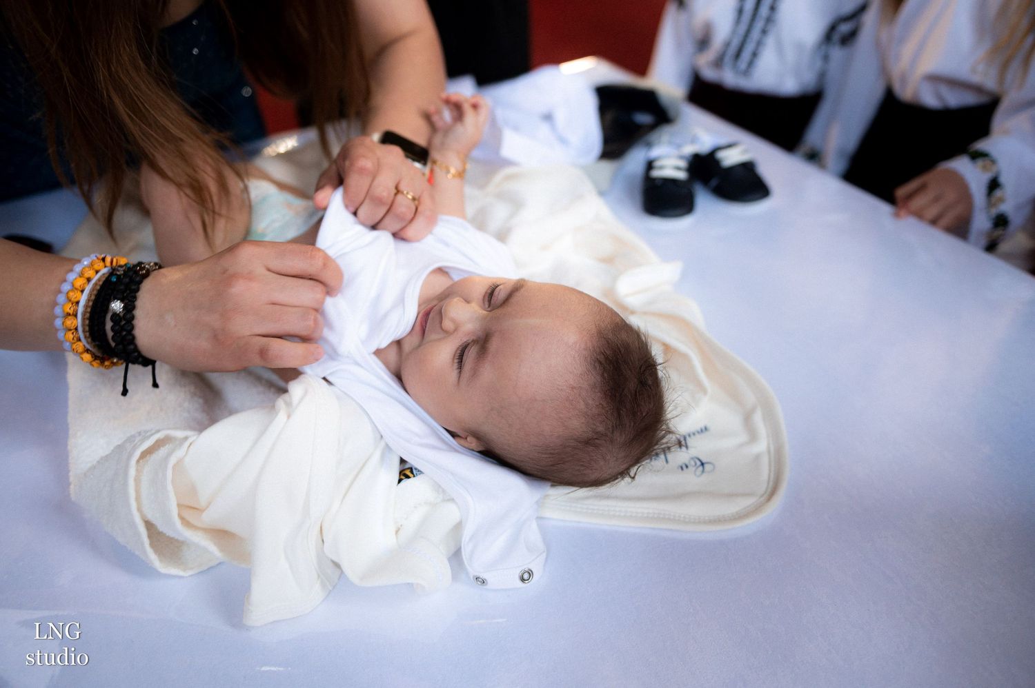 Baby in white baptismal clothing being prepared for Orthodox Christian ceremony.