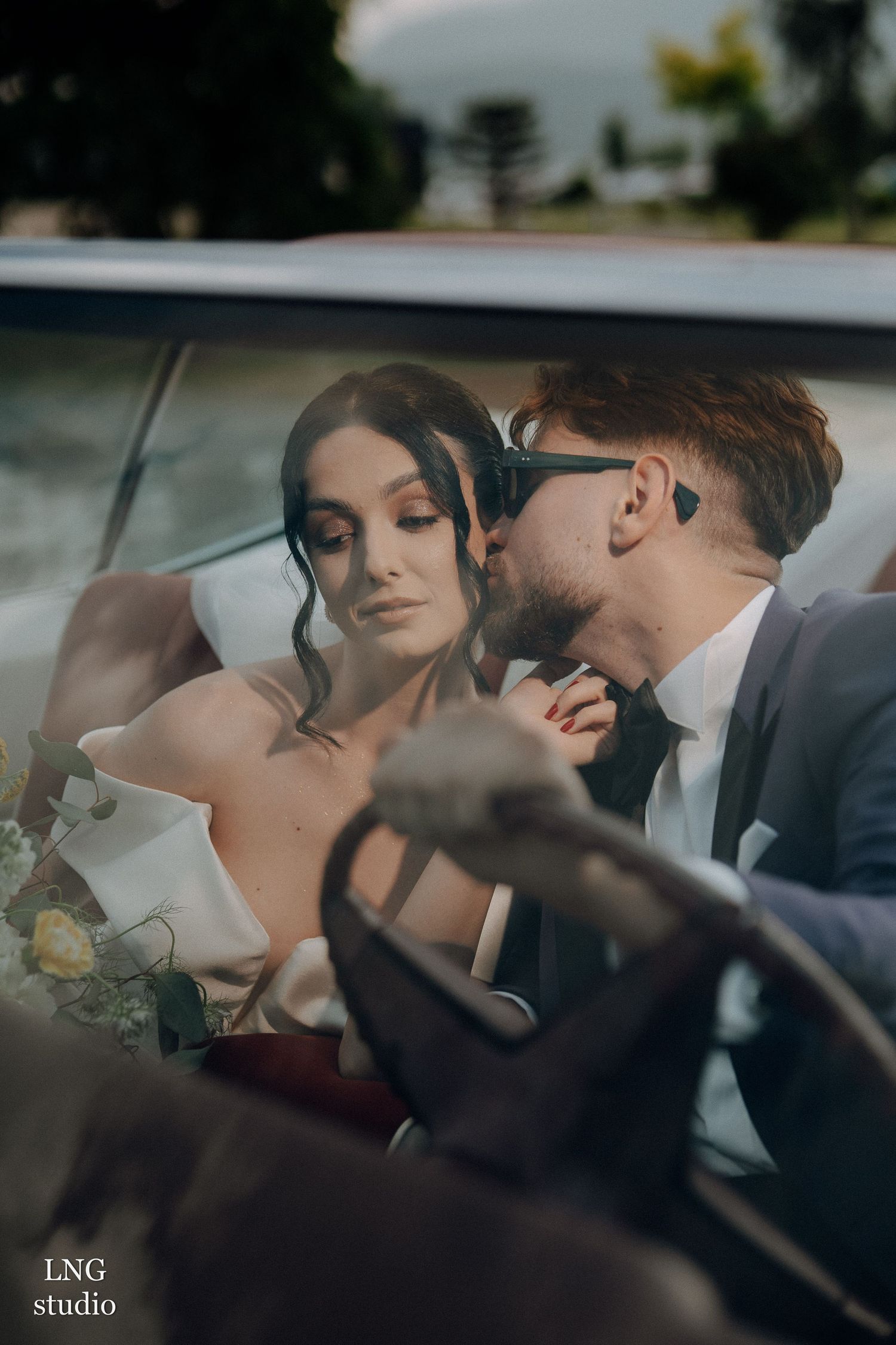 A romantic wedding couple shares an intimate moment together in the back seat of a car.