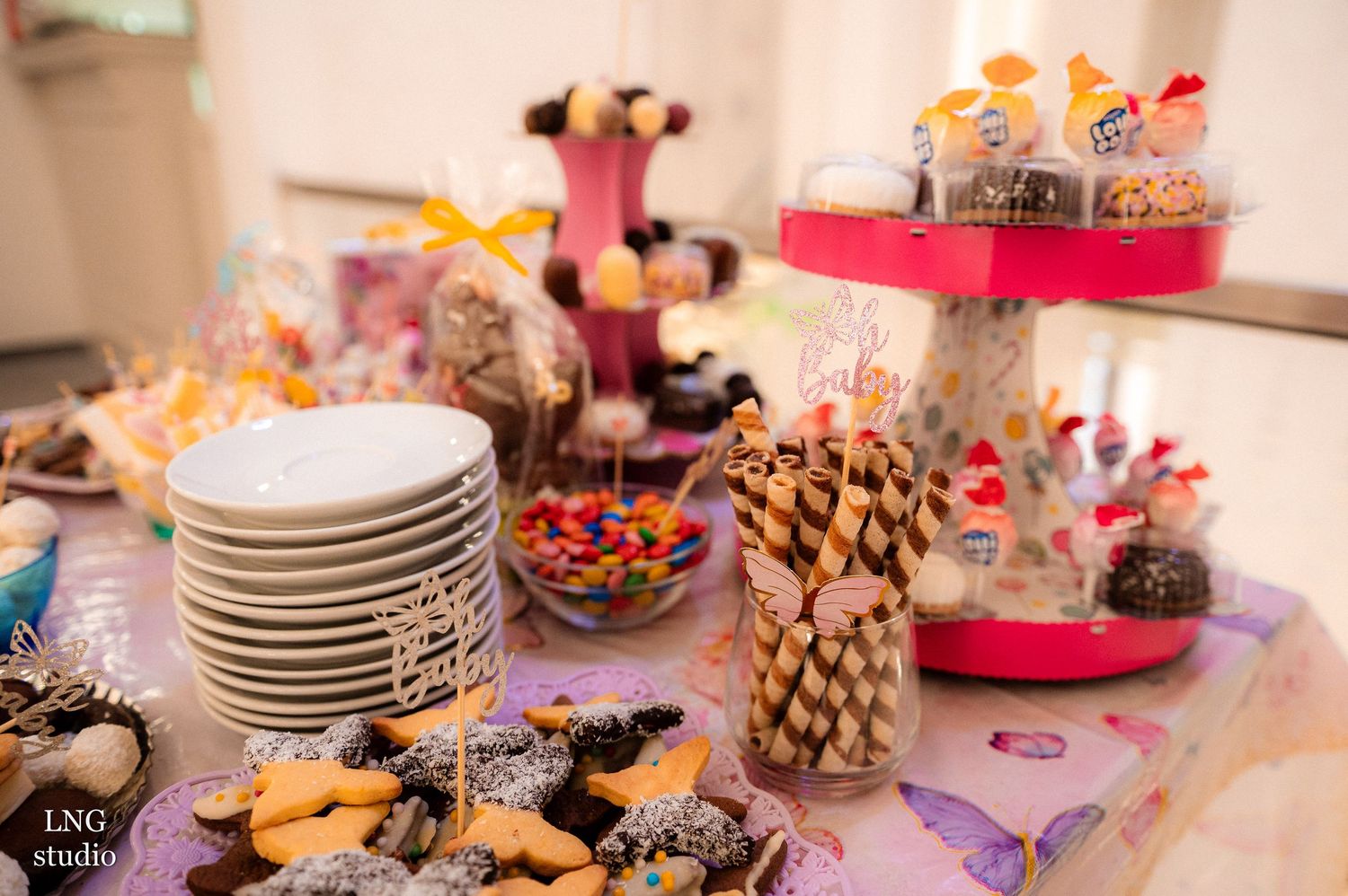 Festive party table spread with various desserts, pastries and stacked plates.