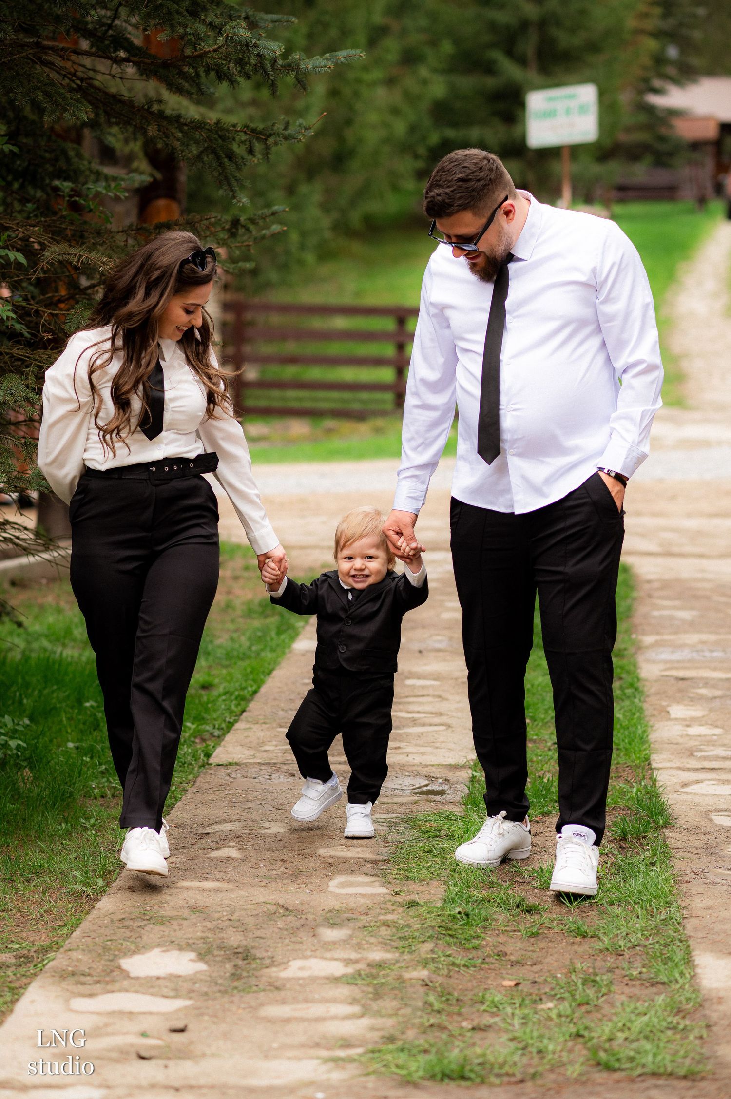 Family walking and playing together on a wooded path in matching formal attire.
