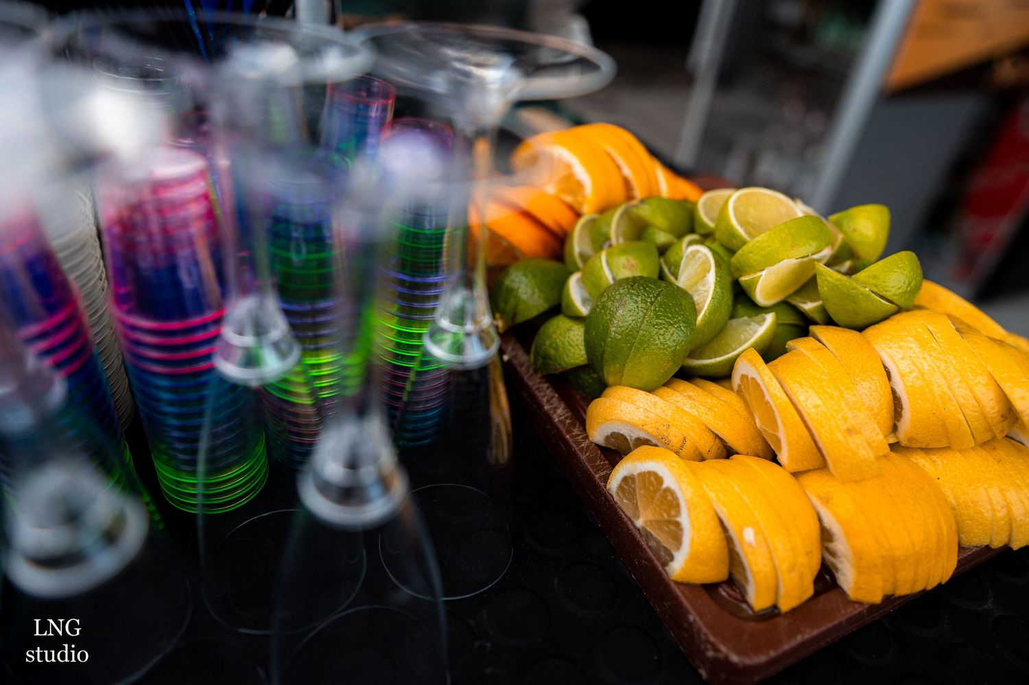 Colorful plastic cups and sliced lemons arranged on a dark surface in a bar setting.