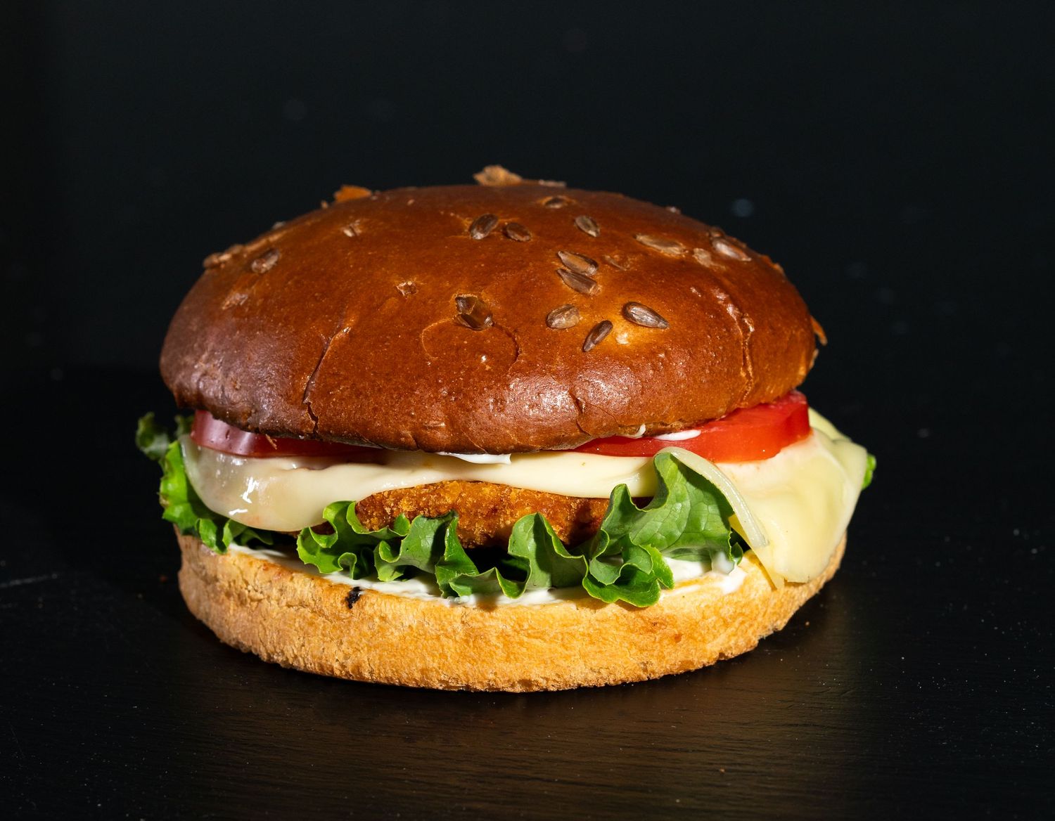 Gourmet burger with fresh vegetables and cheese on a sesame bun against black background.
