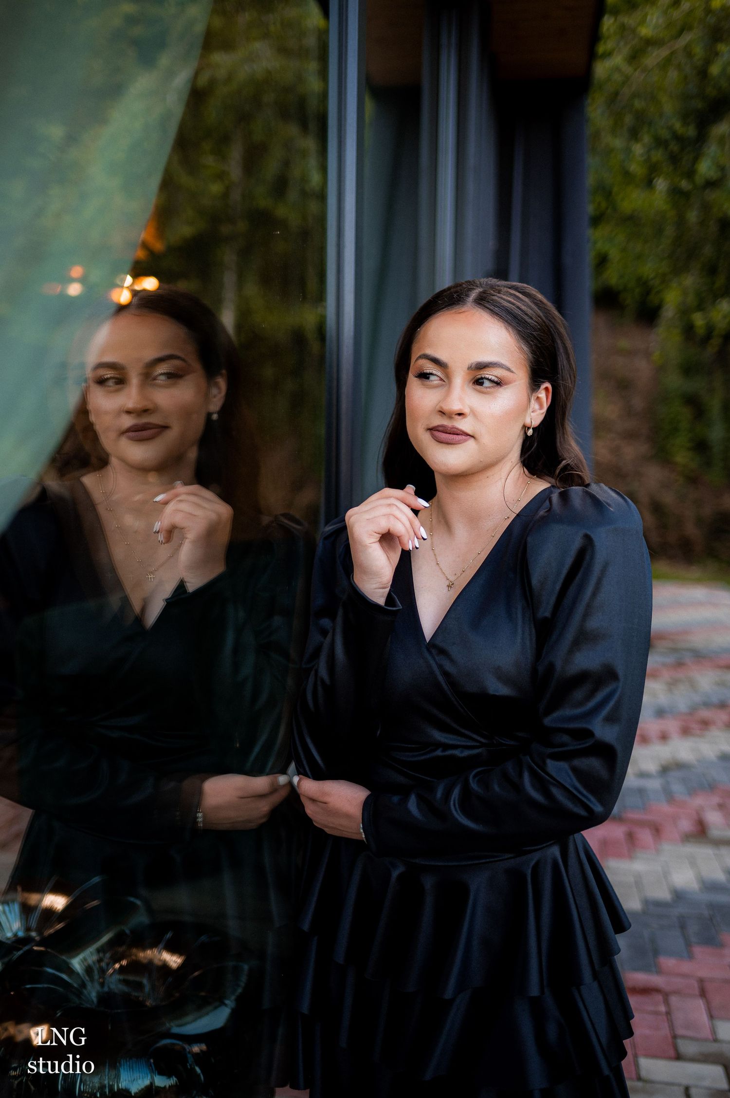 Portrait in black silk dress reflected in window glass during golden hour outdoor photoshoot.