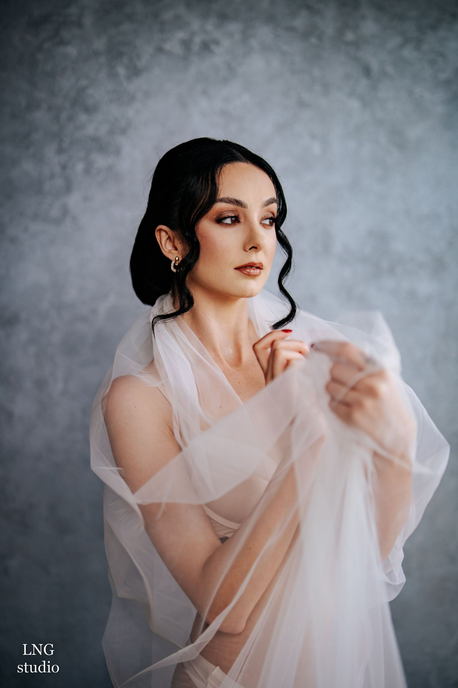 Ethereal portrait featuring delicate fabric draping and soft lighting against a textured grey background.