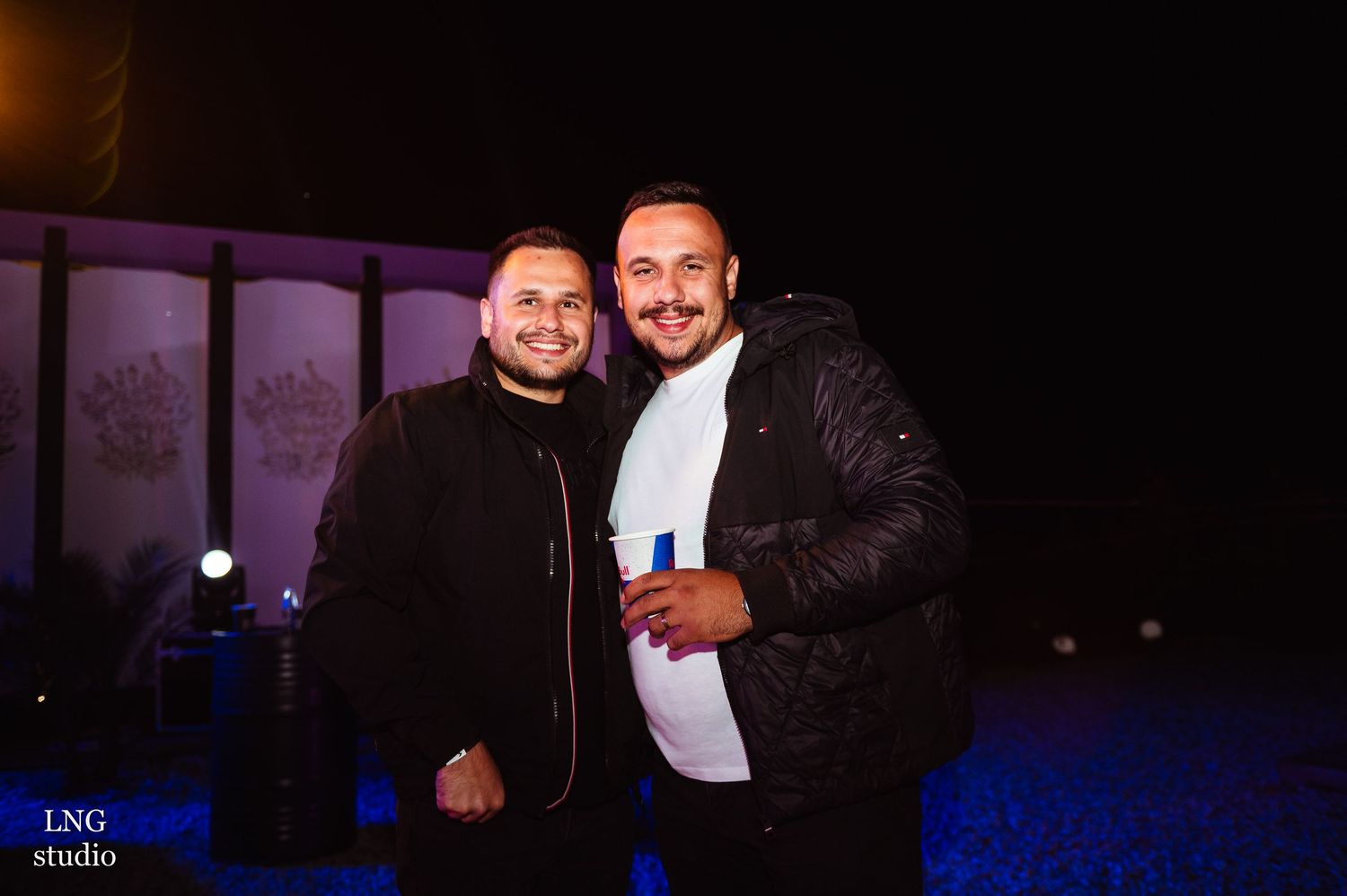 Two people posing outside a venue at night with blue lighting in the background.