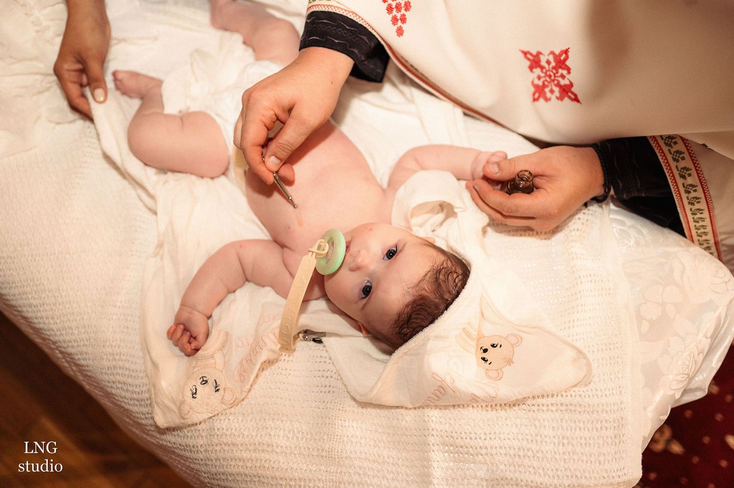 An infant being prepared for a baptism ceremony on white fabric with religious symbols.